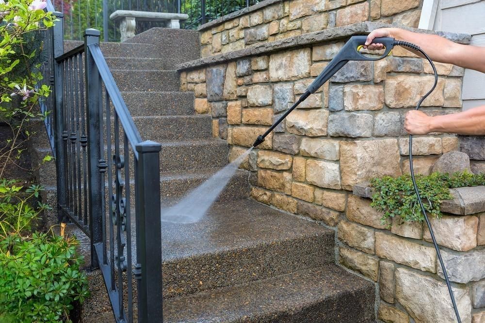 A man is using a high pressure washer to clean the steps of a stone wall.