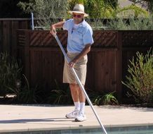 A man is cleaning a swimming pool with a broom.