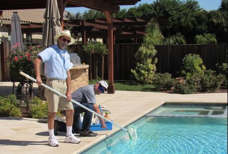 Two men are cleaning a swimming pool with a broom