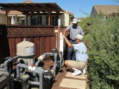 Two men are working on a pool pump in a backyard.