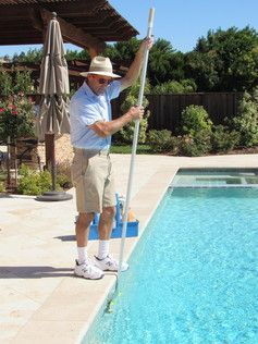 A man is cleaning a swimming pool with a broom.