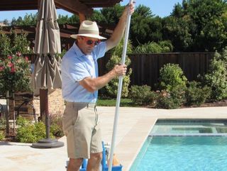 A man in a hat is cleaning a pool with a mop