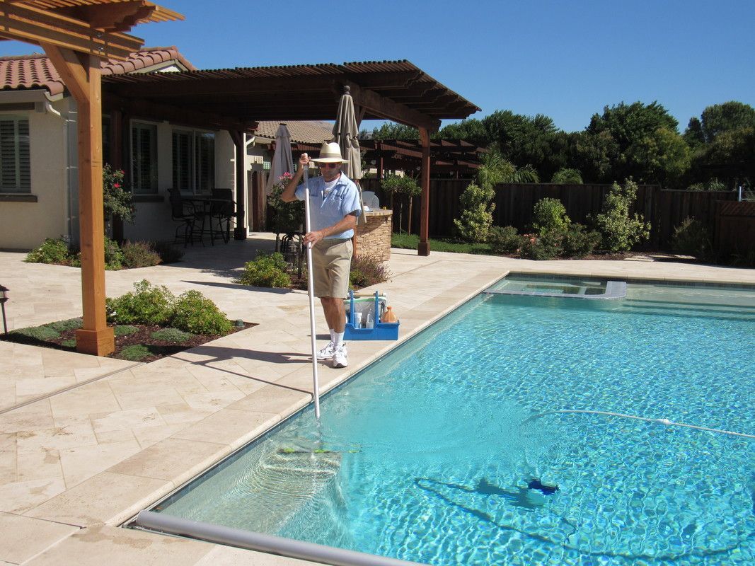 A man in a hat is standing next to a swimming pool.