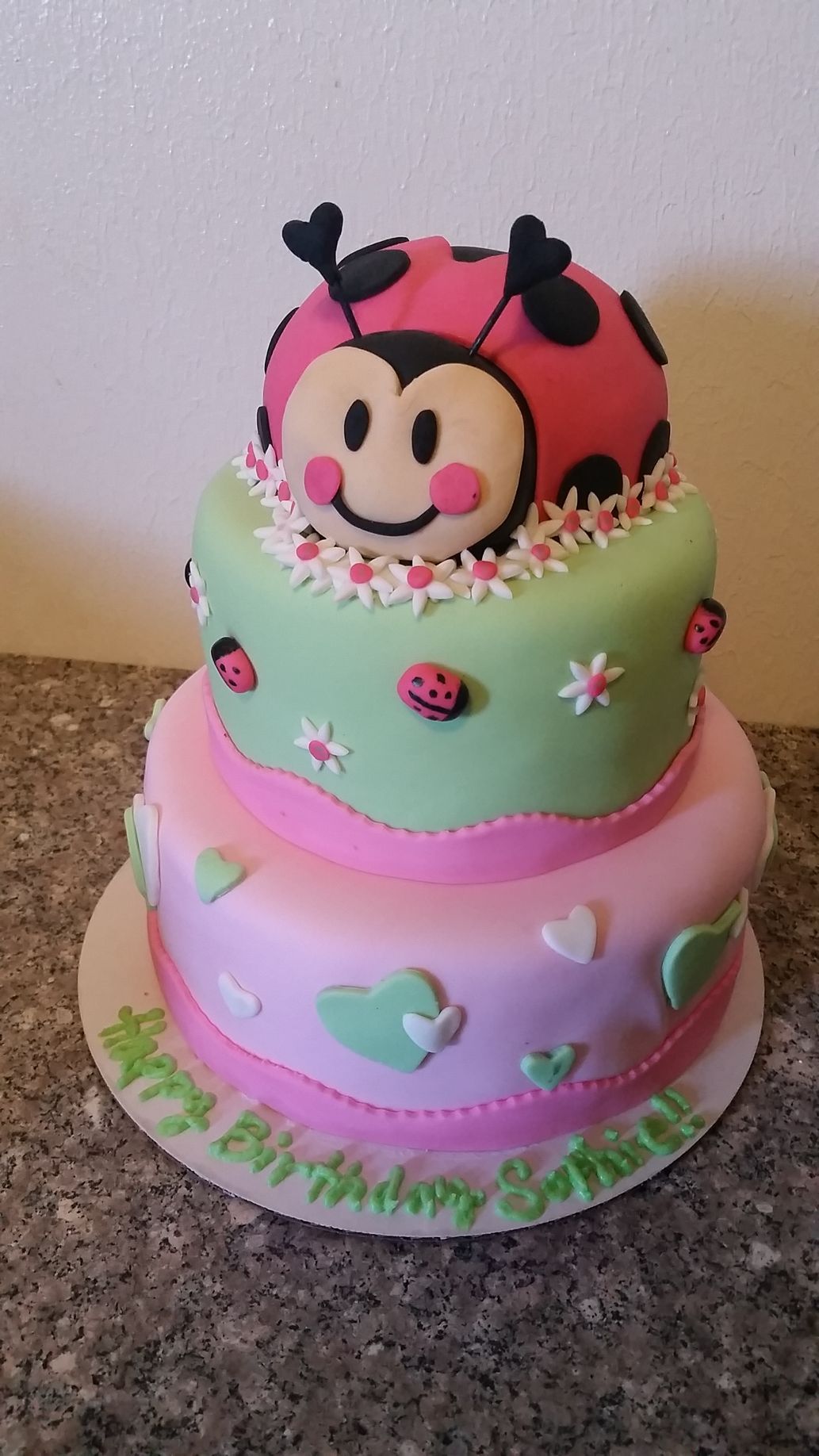 A pink and green birthday cake with a ladybug on top