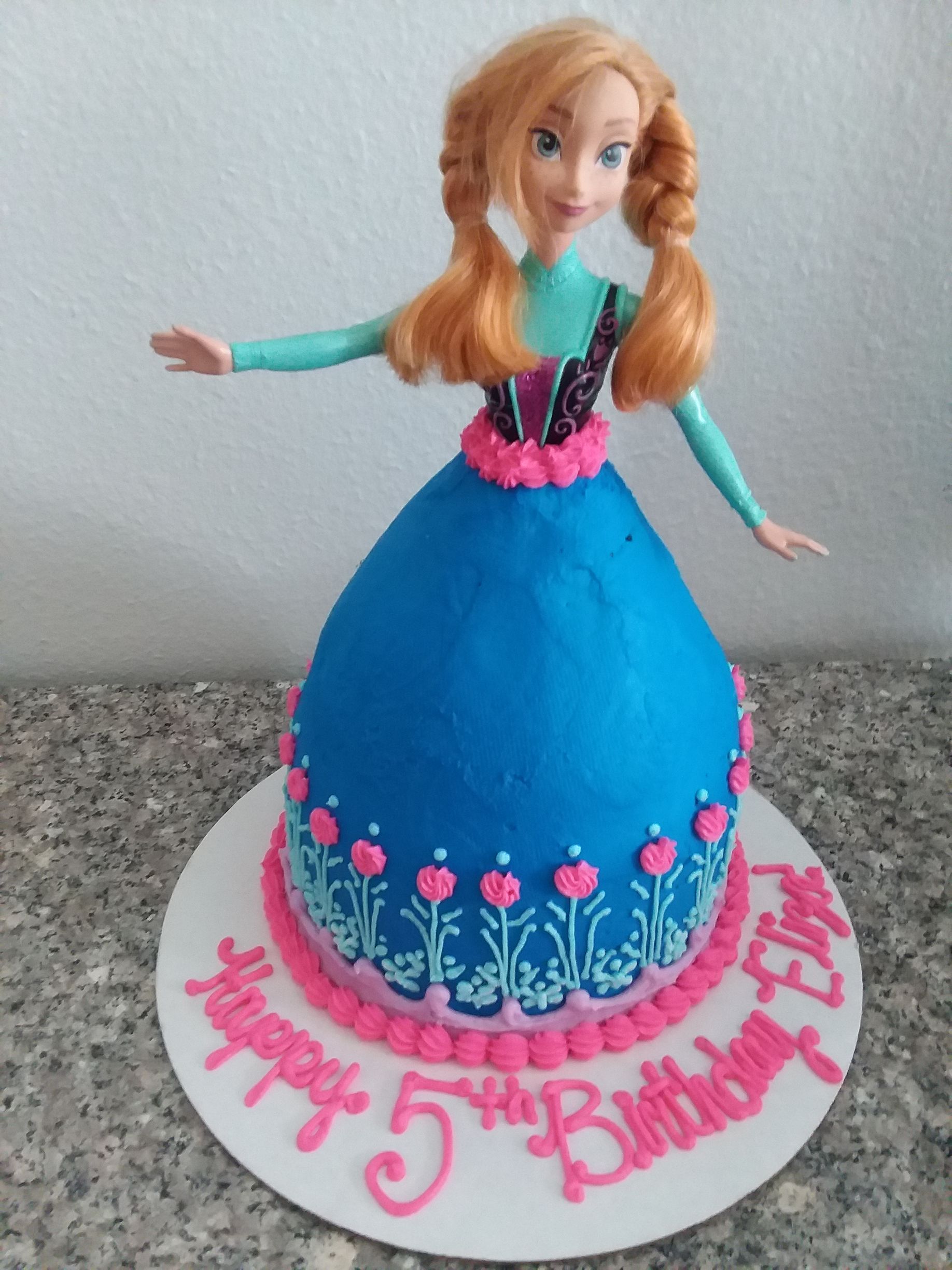 A cake with a doll on it that says happy 5th birthday