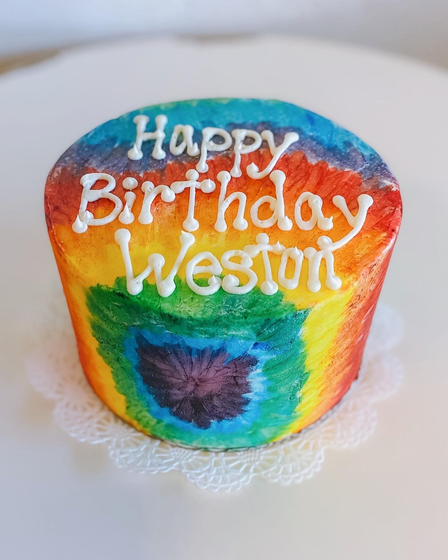 A rainbow colored cake that says happy birthday weston