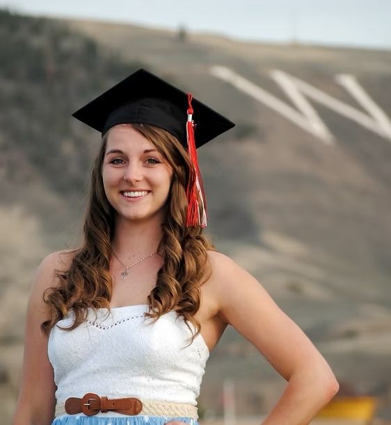 A woman wearing a graduation cap and gown is smiling