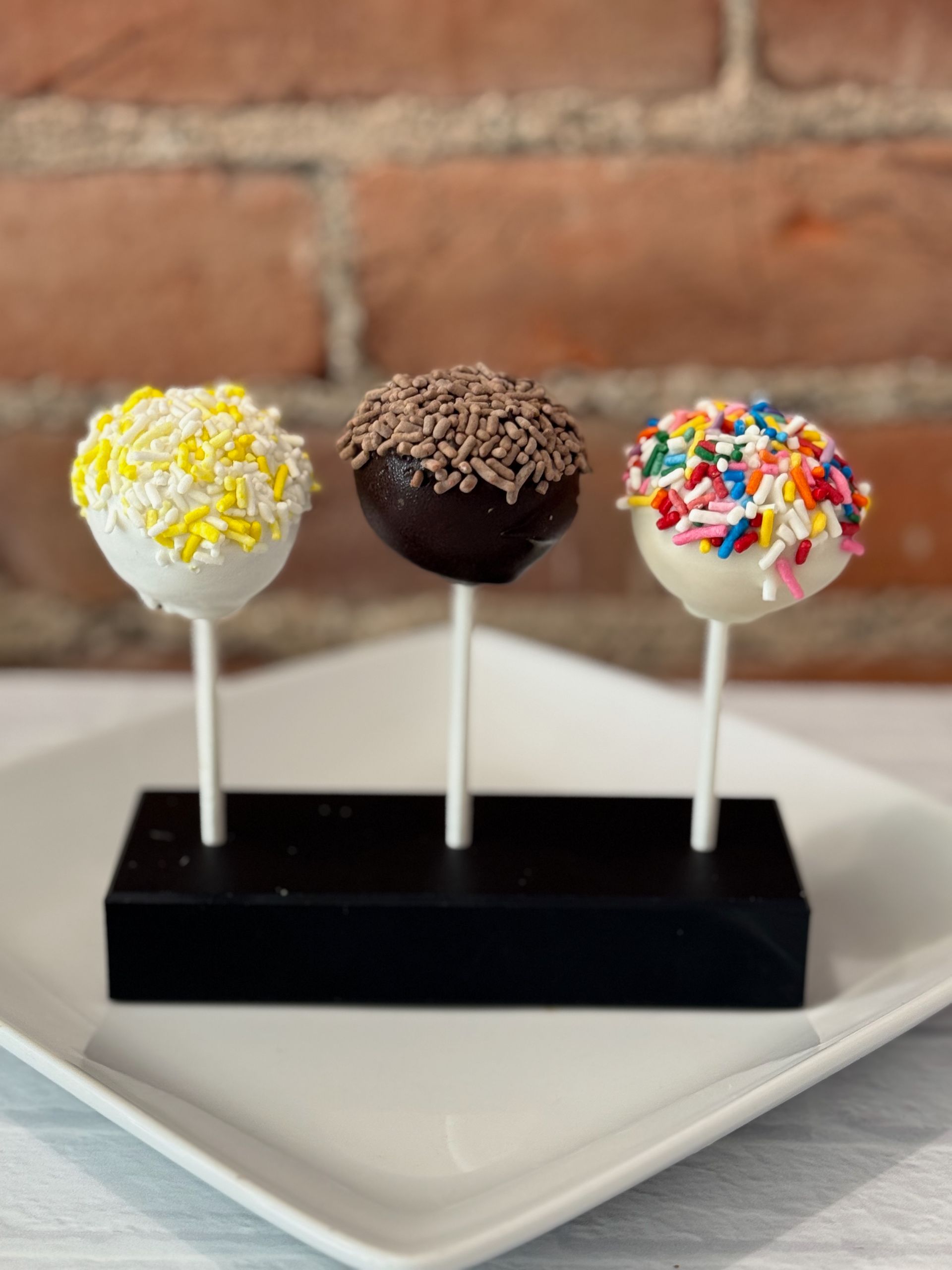 Three cake pops are sitting on a white plate.