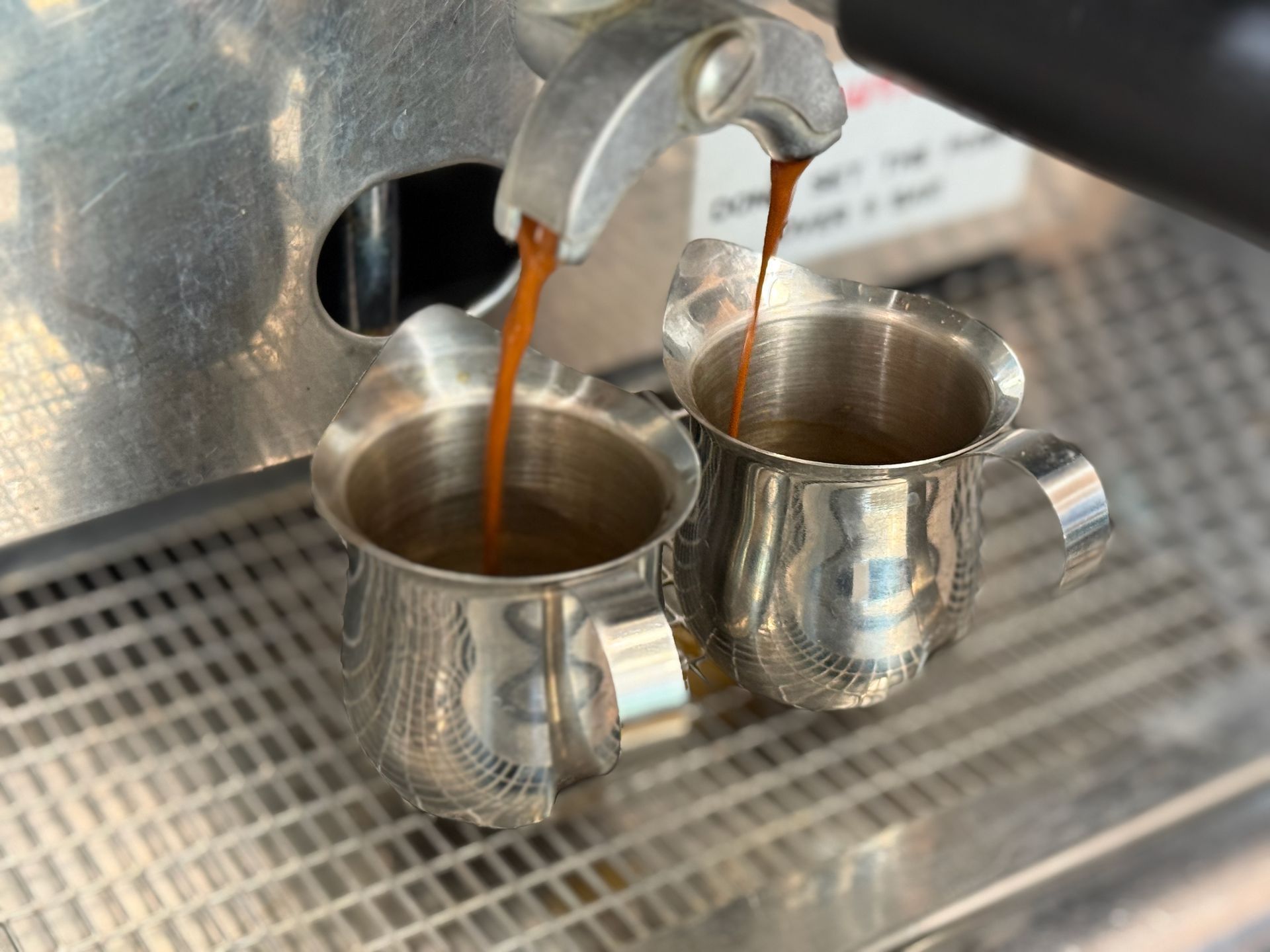 Two cups of coffee are being poured into a coffee machine.