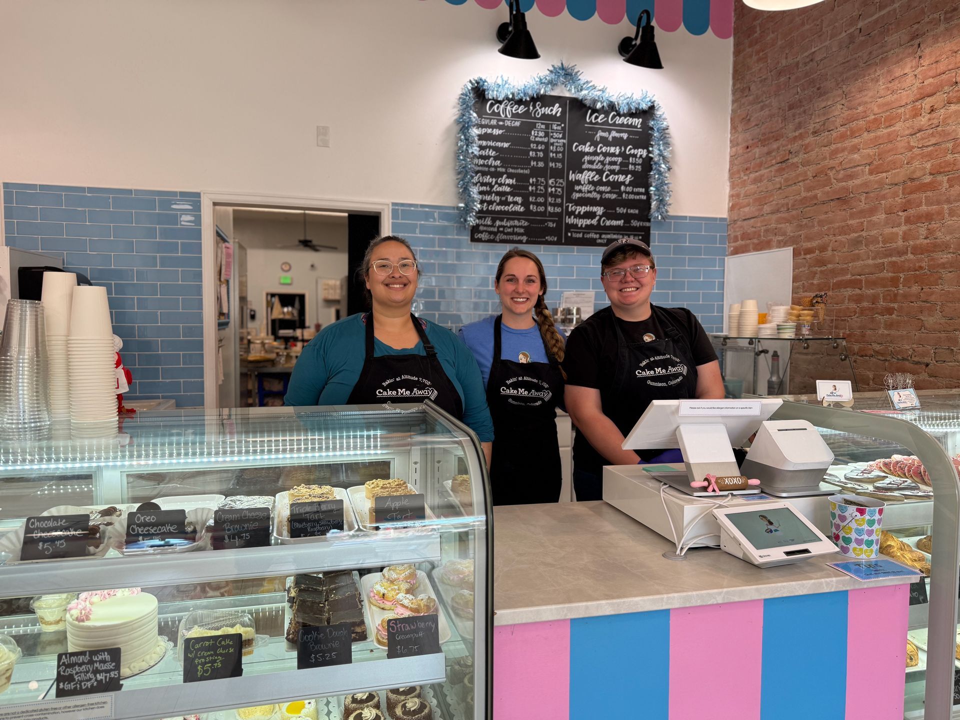 Three people are standing in front of a display case in a bakery.