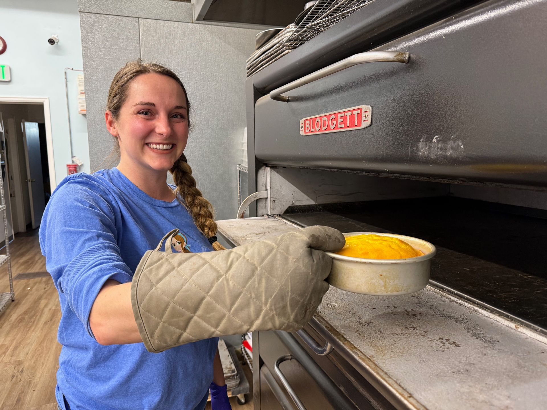 A woman in a blue shirt is holding a pan of food in front of an oven.