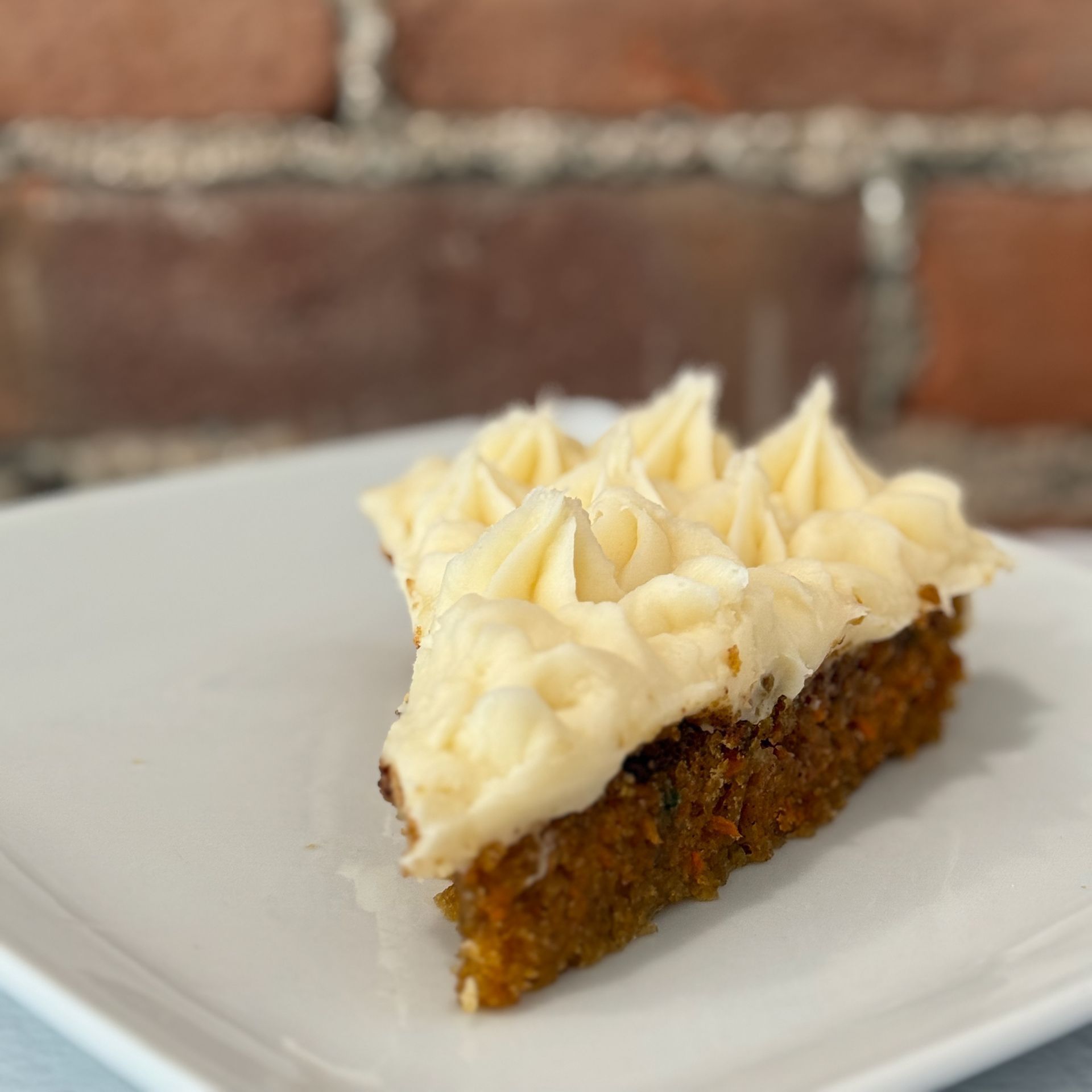 A slice of carrot cake with white frosting on a white plate.