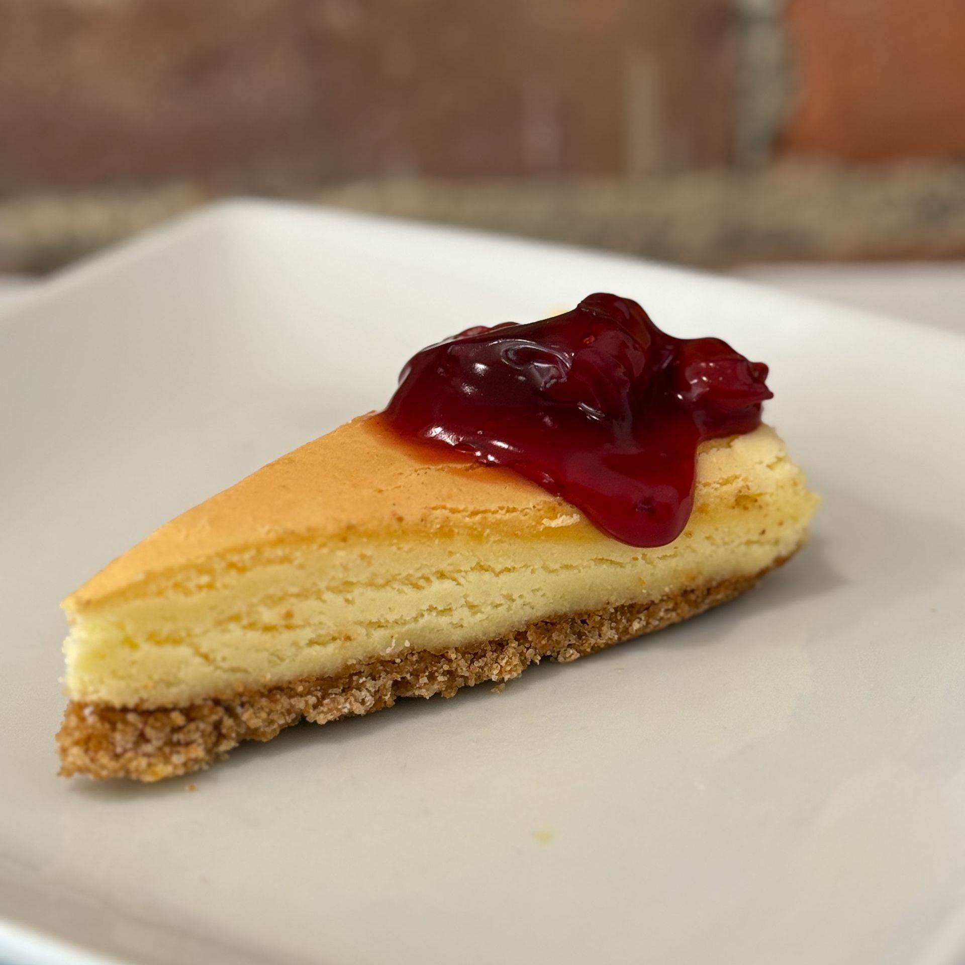 A slice of cheesecake with raspberry sauce on top on a white plate