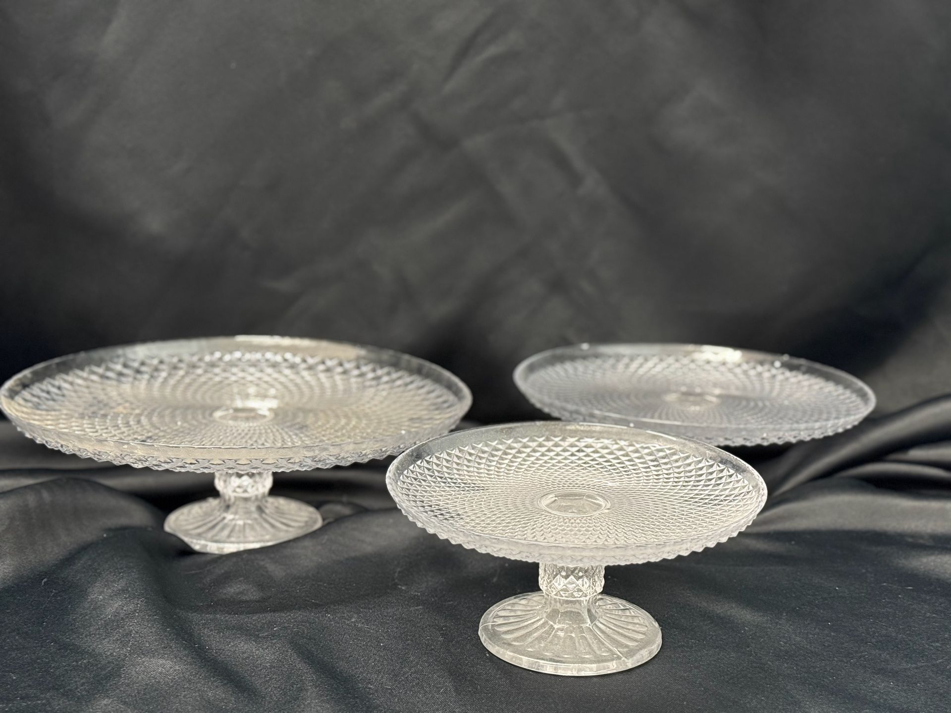 Three clear glass cake stands are sitting on a black cloth.