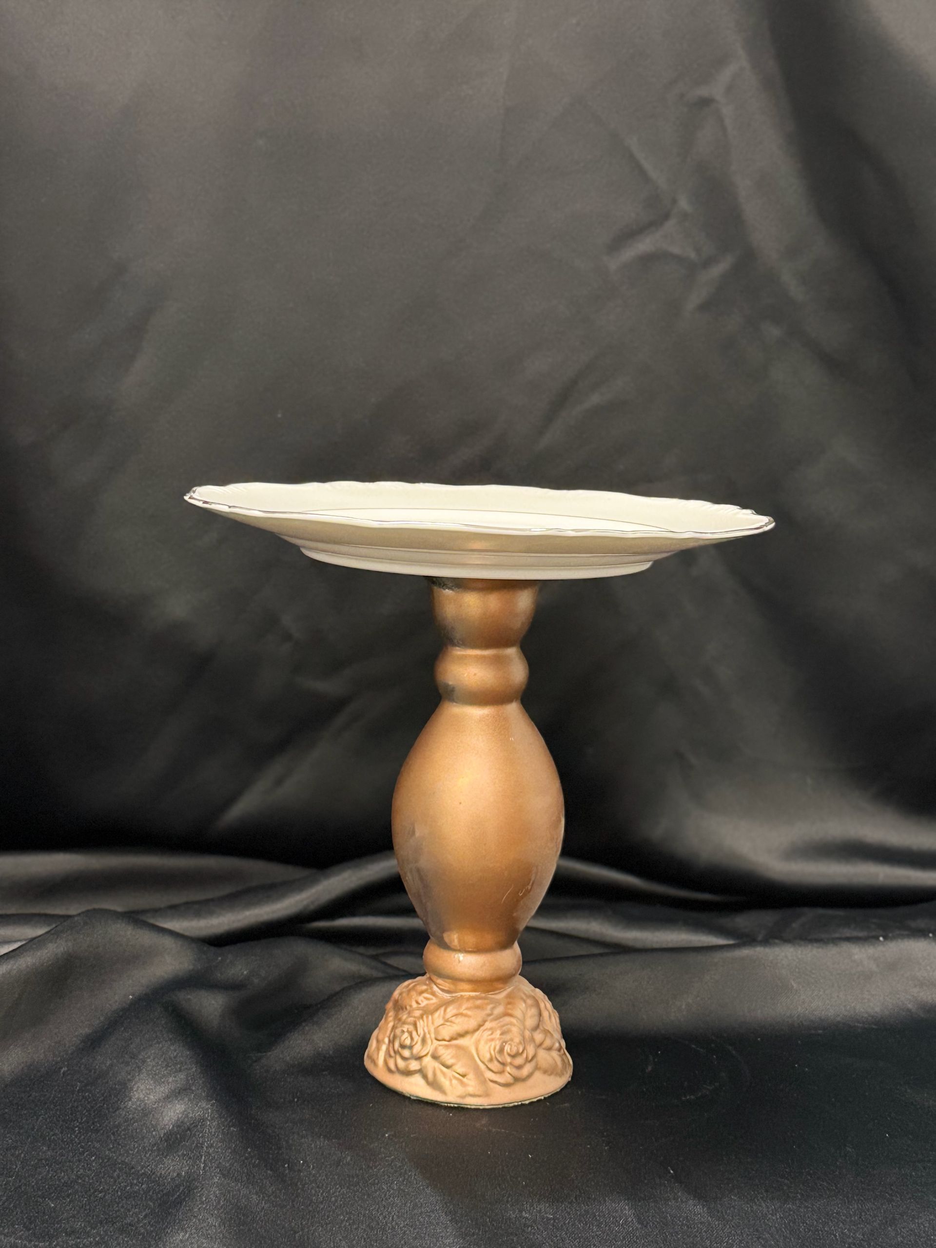 A gold cake stand with a white plate on it