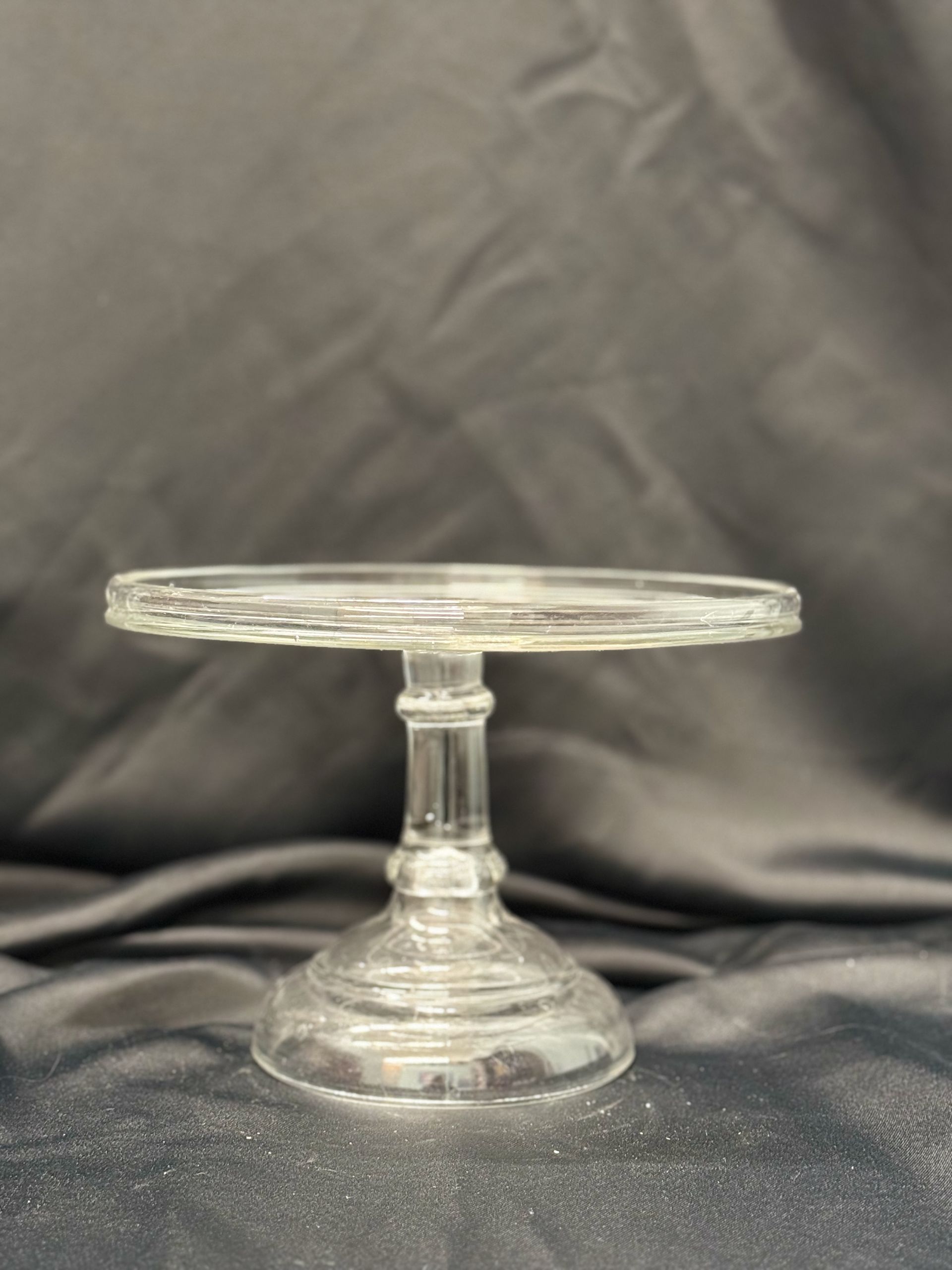 A clear glass cake stand is sitting on a black cloth.