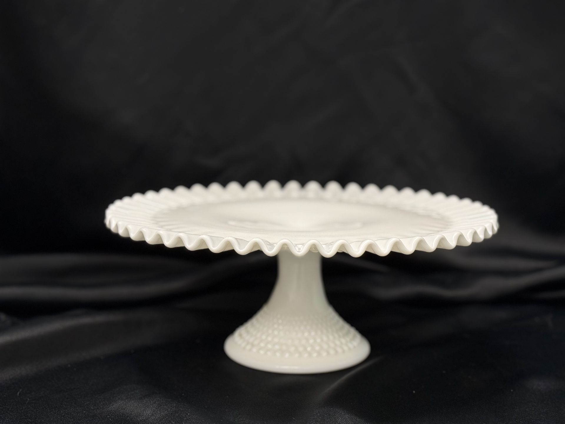 A white cake stand is sitting on top of a black cloth.