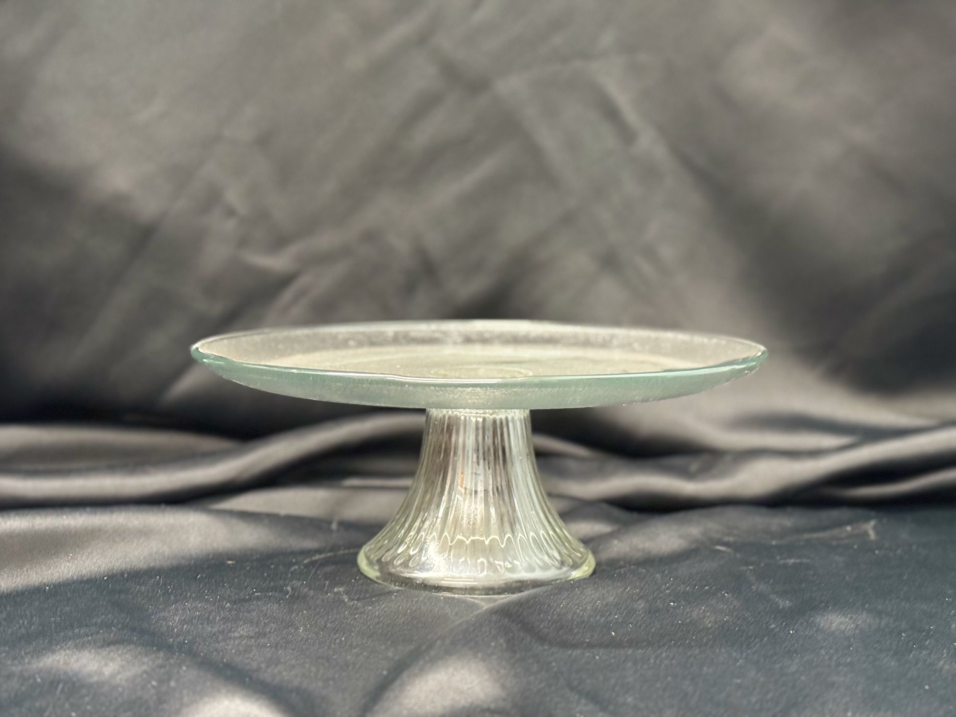 A clear glass cake stand is sitting on a black cloth.