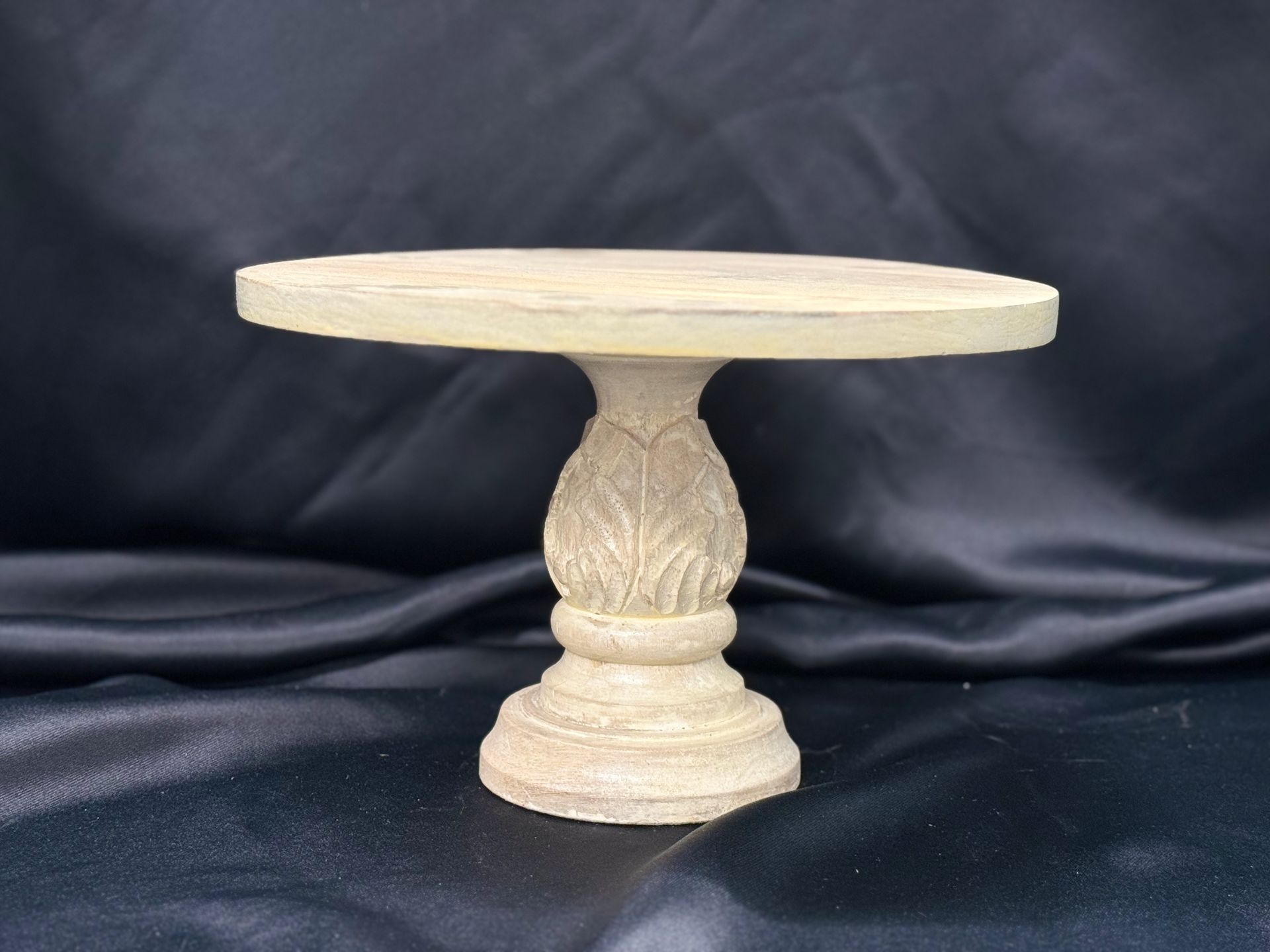 A small white table with a pineapple shaped base is sitting on a black cloth.