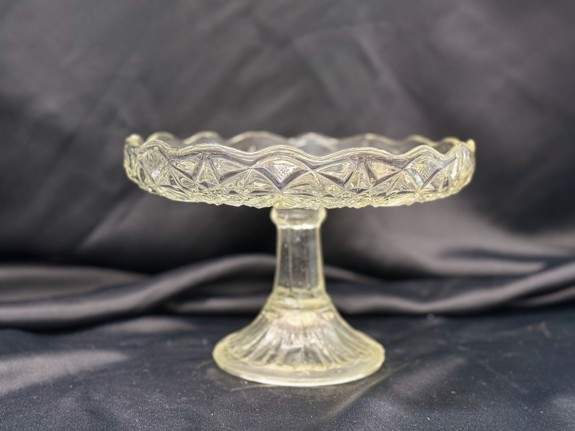 A clear glass cake stand is sitting on a black cloth