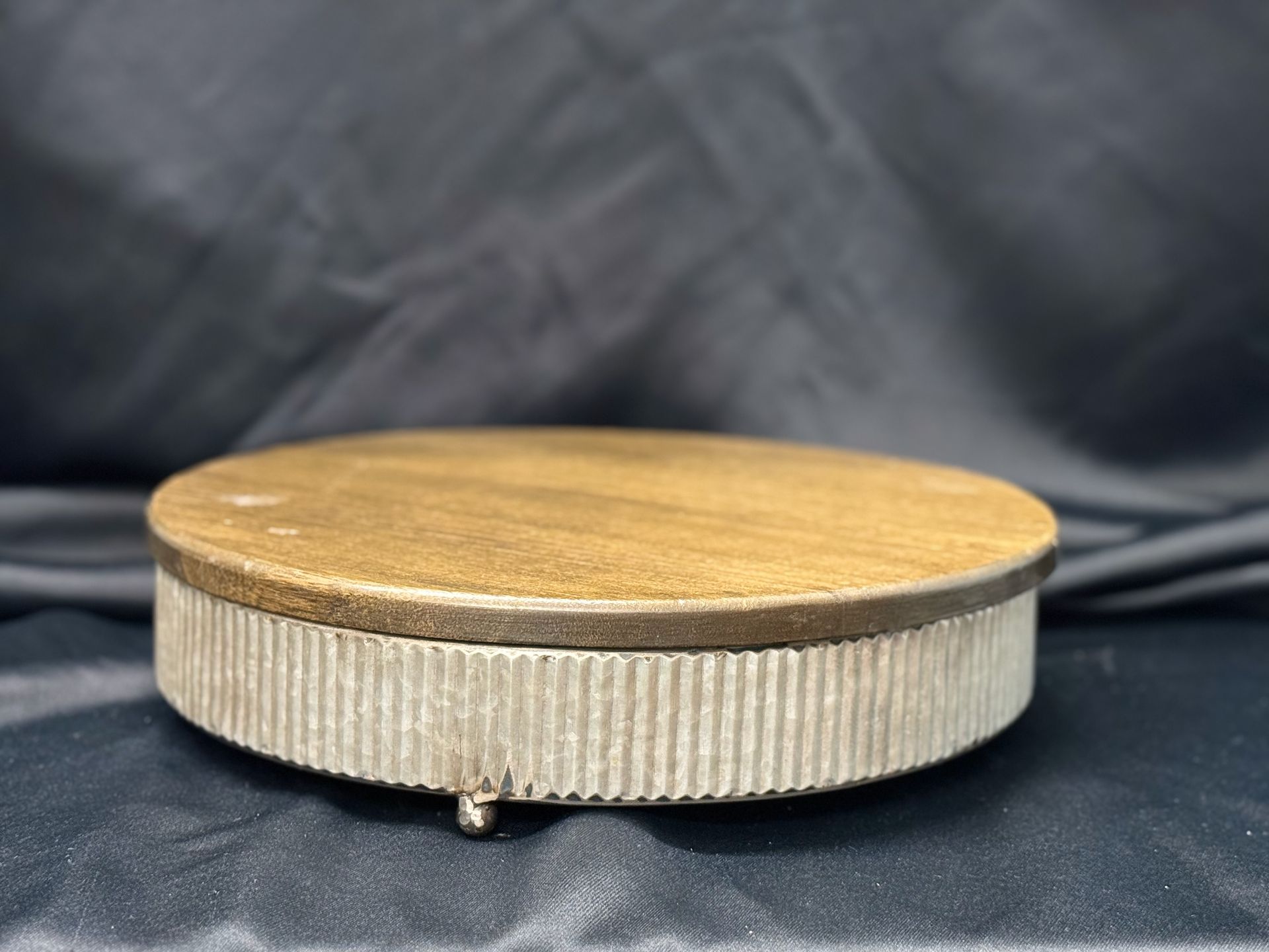 A wooden cake stand with a metal base is sitting on a black cloth.