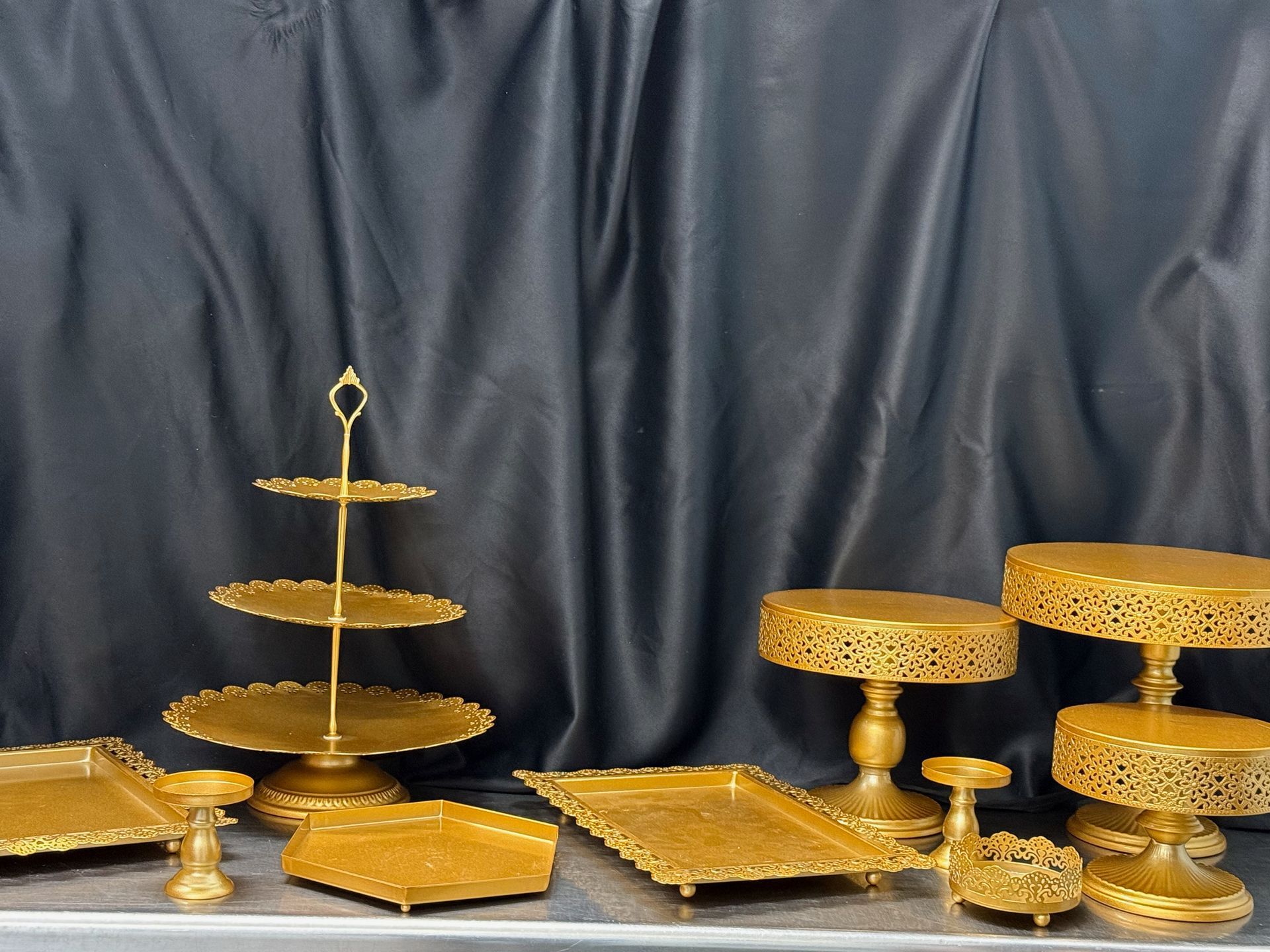 A group of gold cake stands are sitting on a table in front of a black curtain.