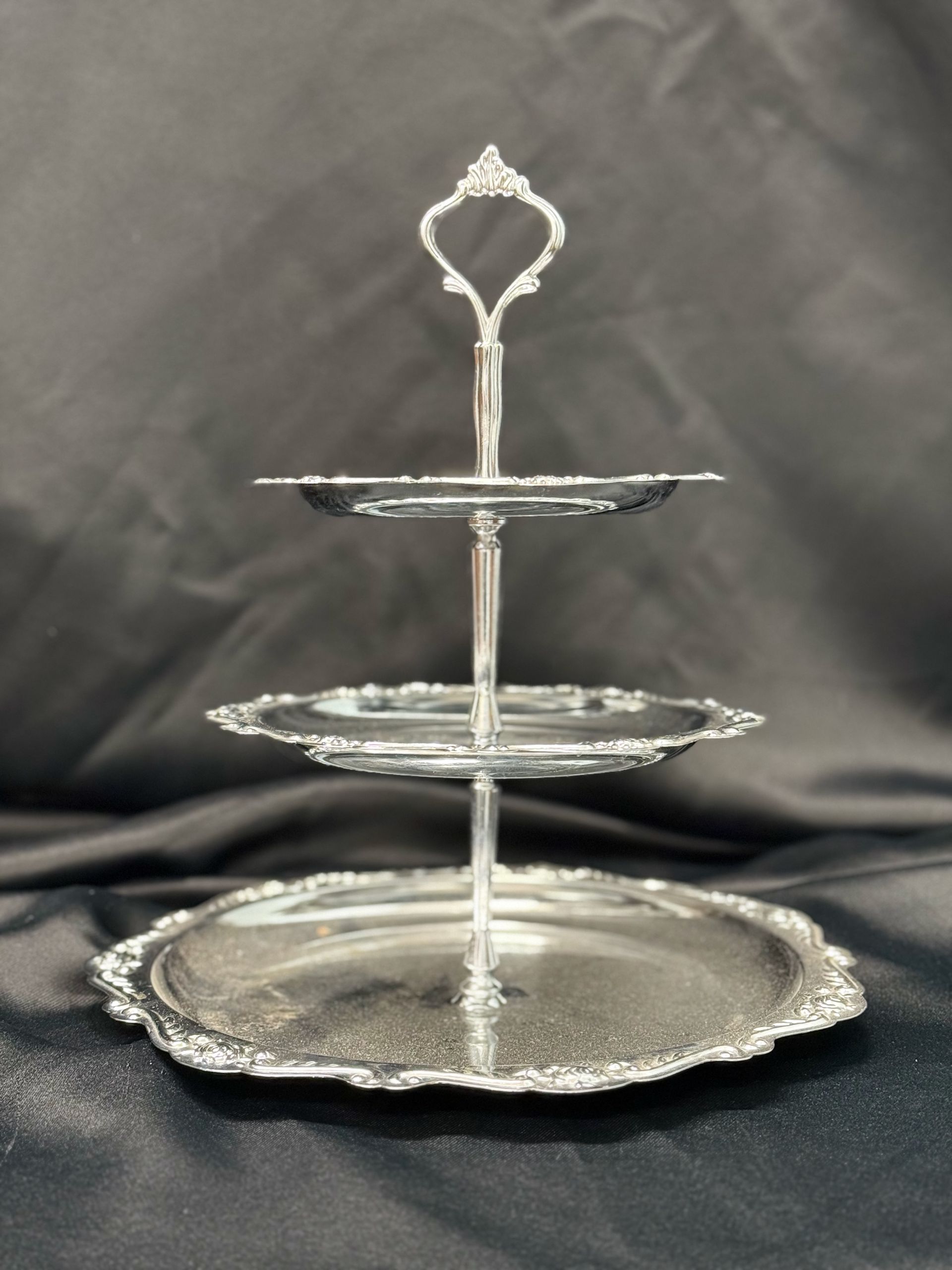 A silver three tiered cake stand with a handle
