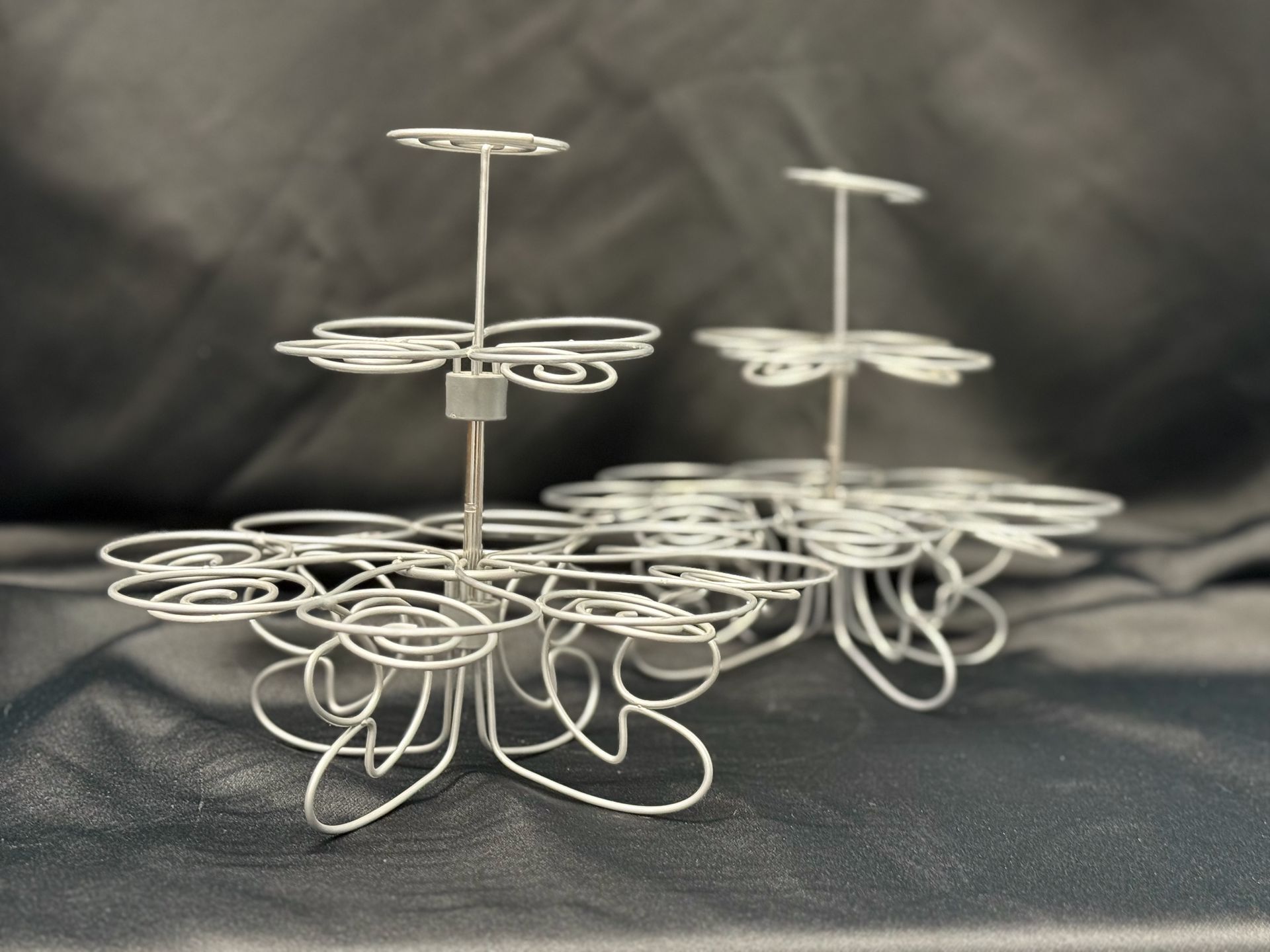 Three white wire cupcake stands are sitting on a black cloth