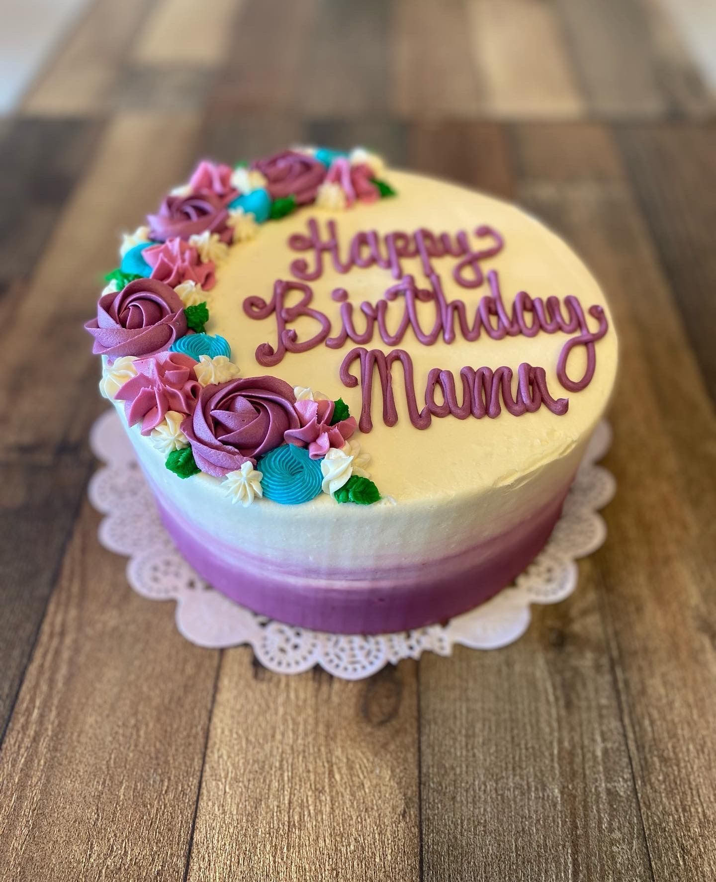 A birthday cake with purple frosting and flowers on a wooden table.
