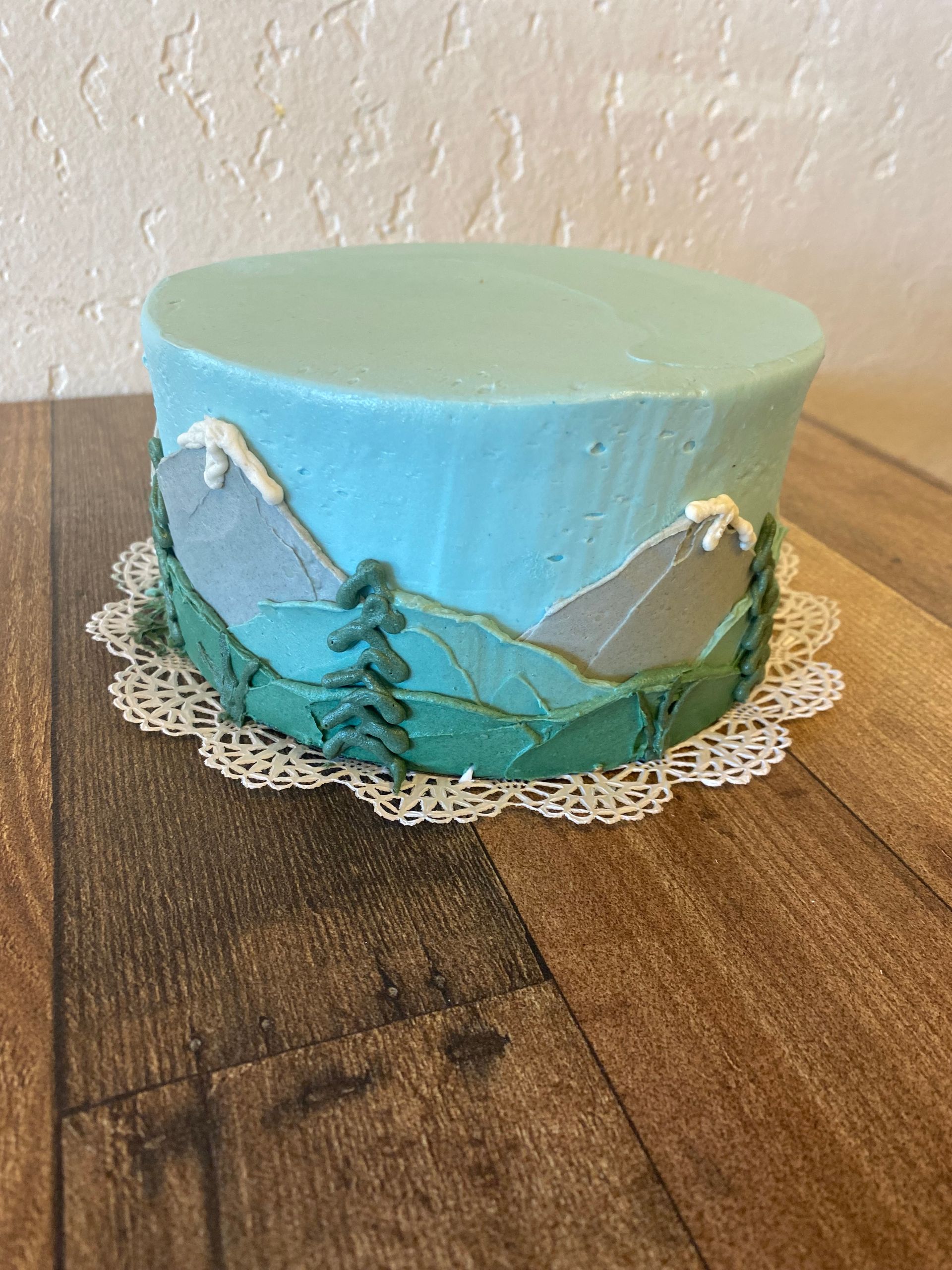 A cake with mountains and trees on it is sitting on a wooden table.
