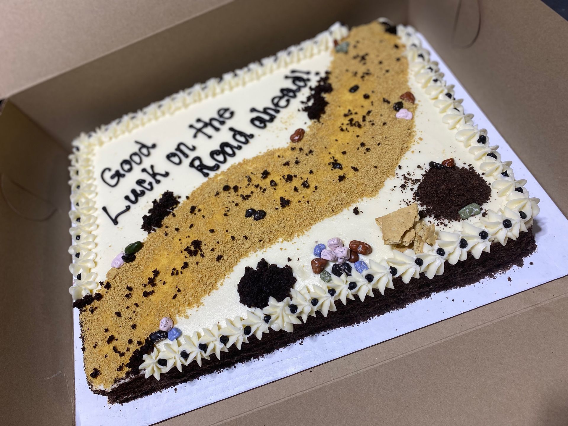 A cake in a box that says good luck on the road ahead