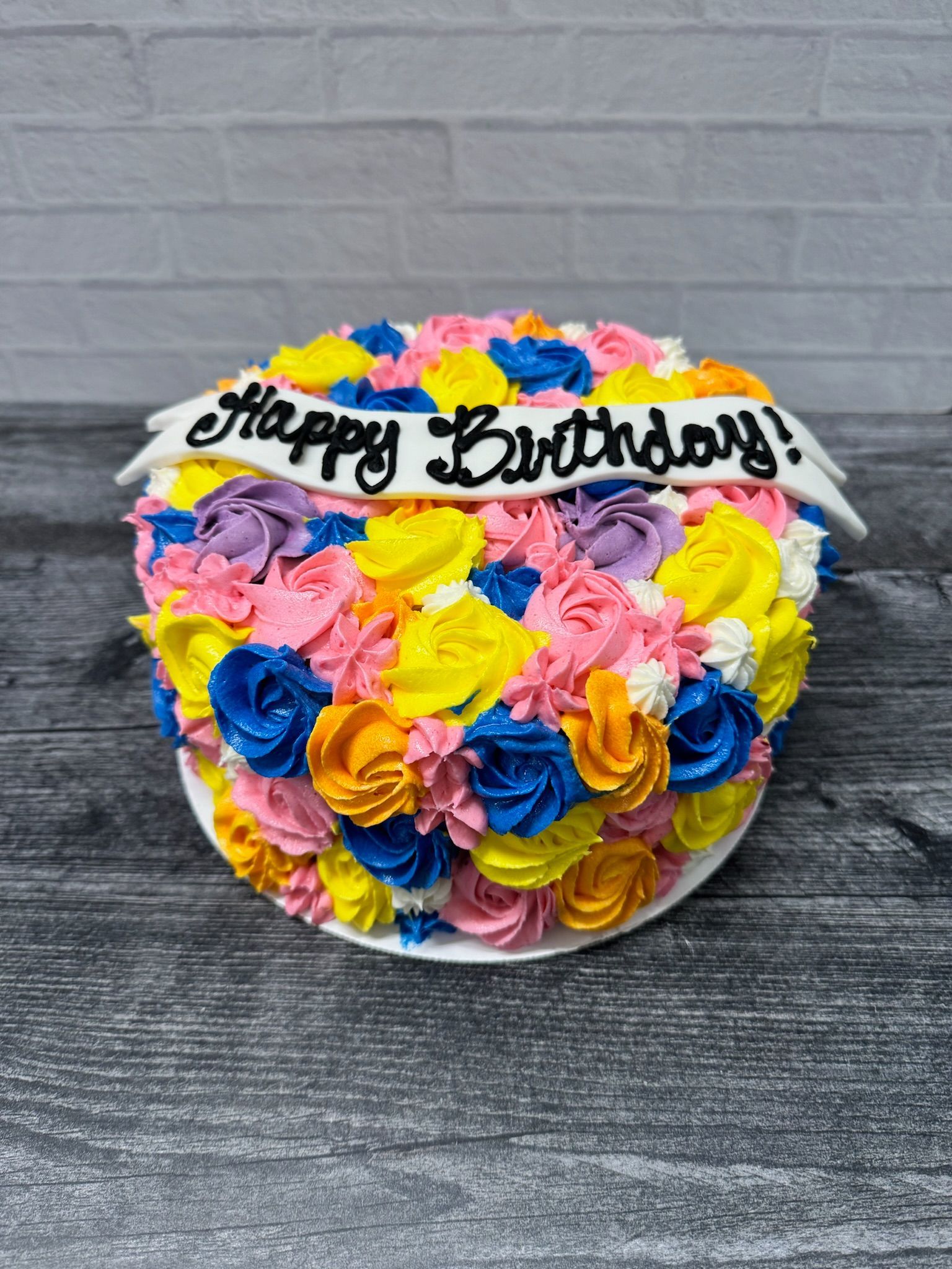 A colorful birthday cake with flowers on it is on a wooden table.