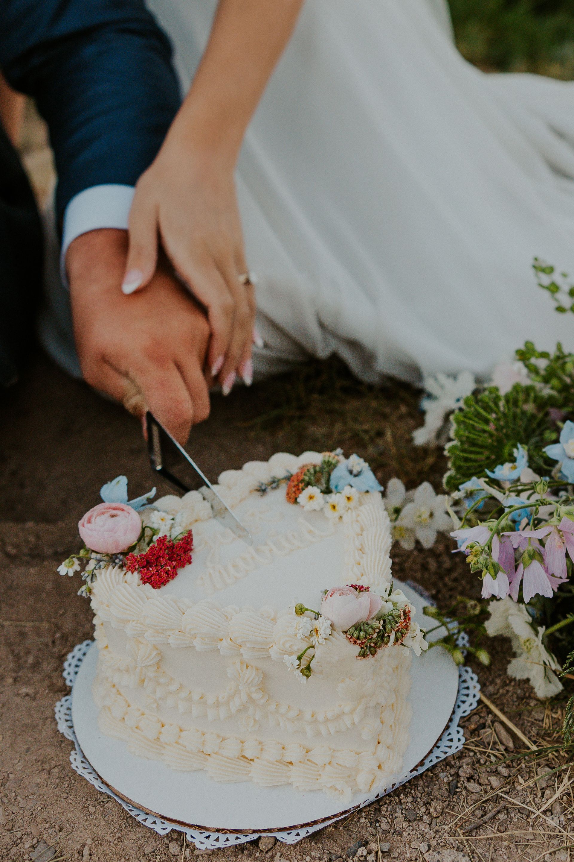 A bride and groom are cutting their wedding cake on the ground.