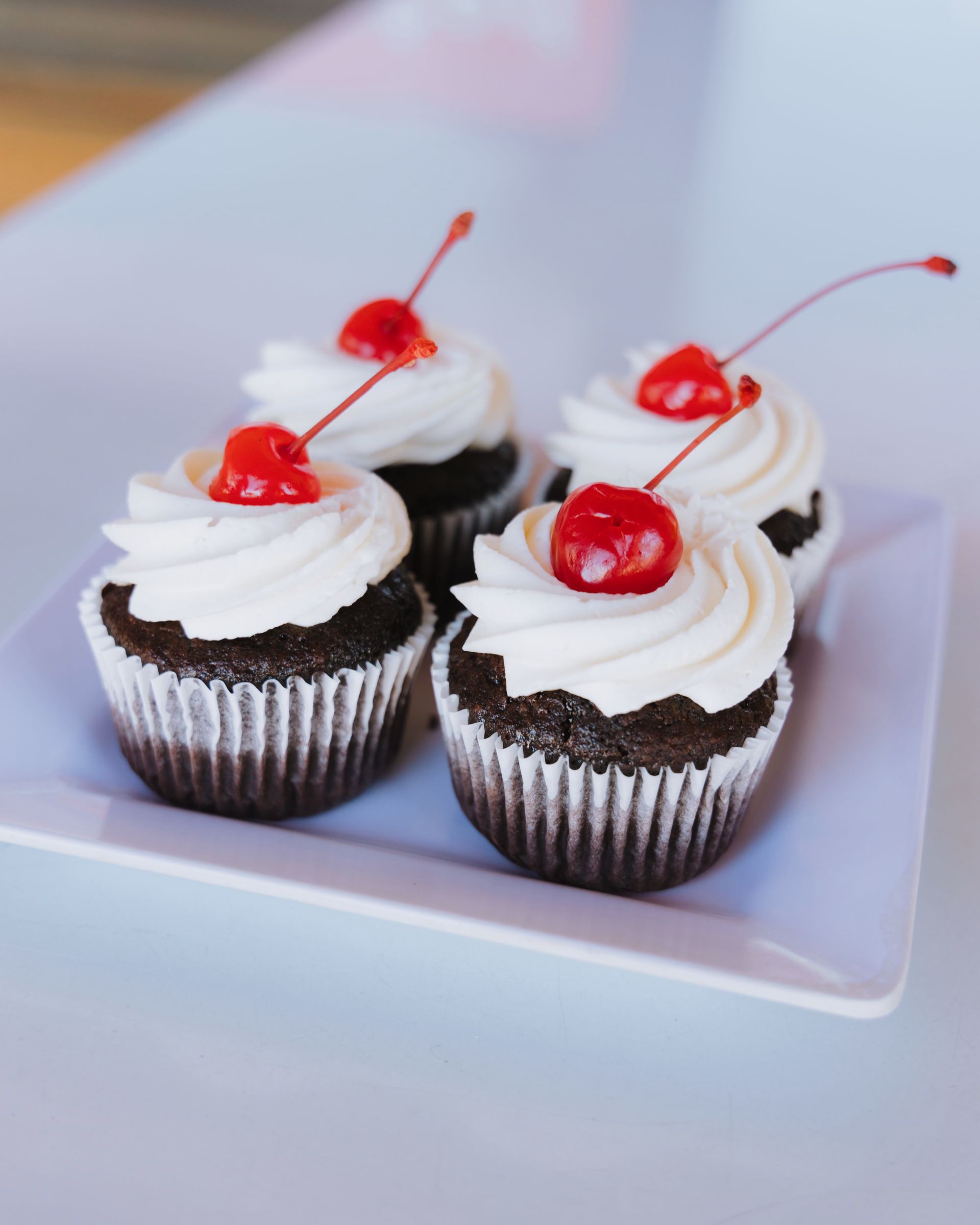 Four chocolate cupcakes with white frosting and cherries on top