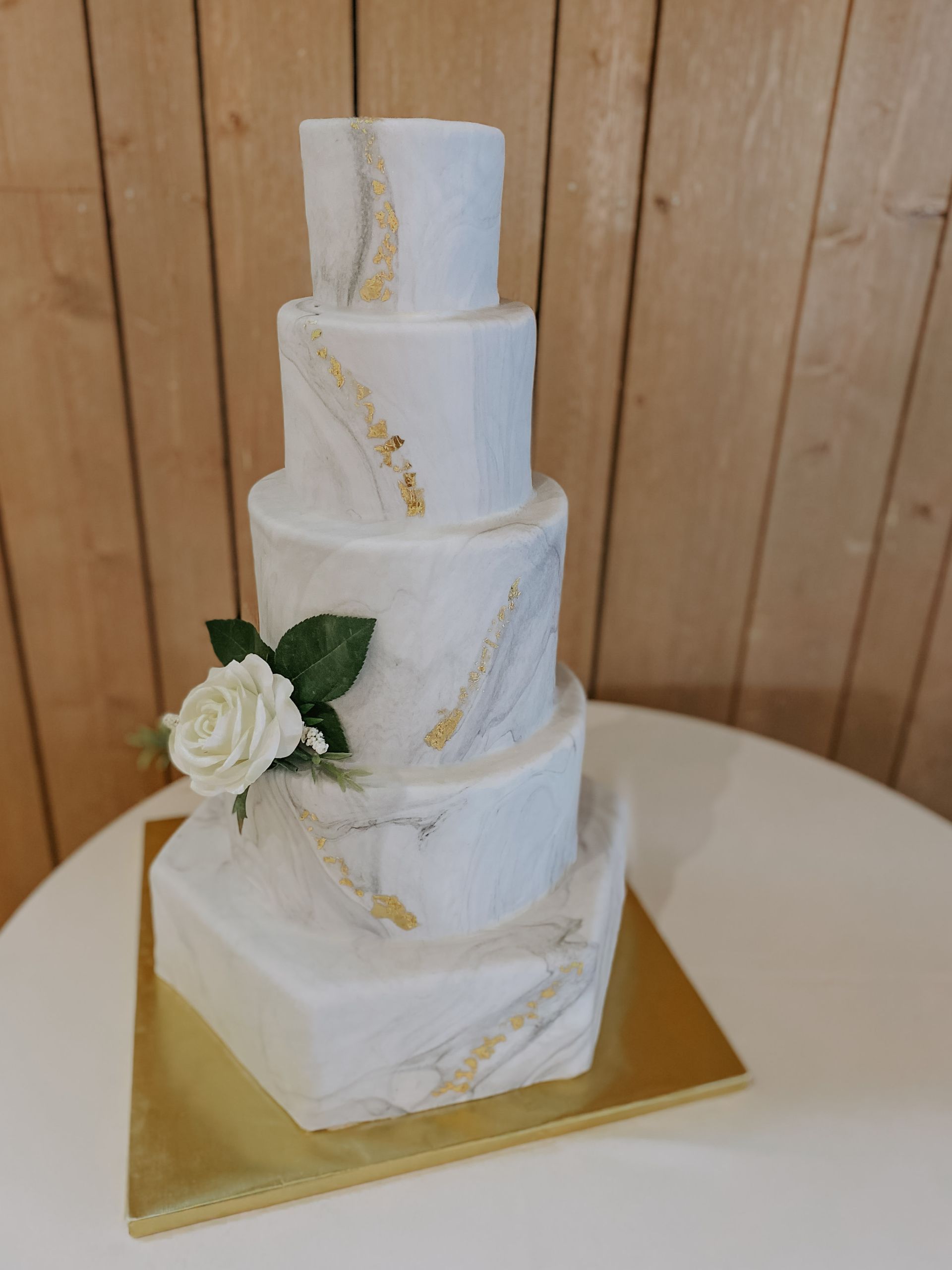 A white marble wedding cake with a white rose on top is sitting on a table.