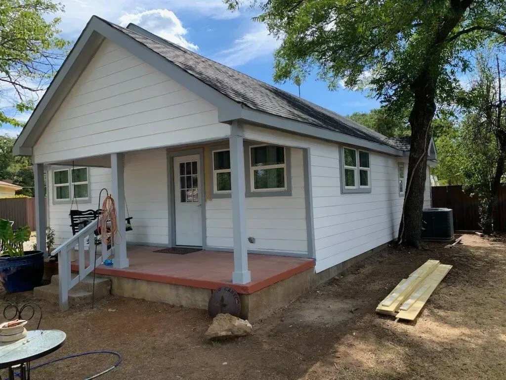 A small white house with a porch and a table in front of it.