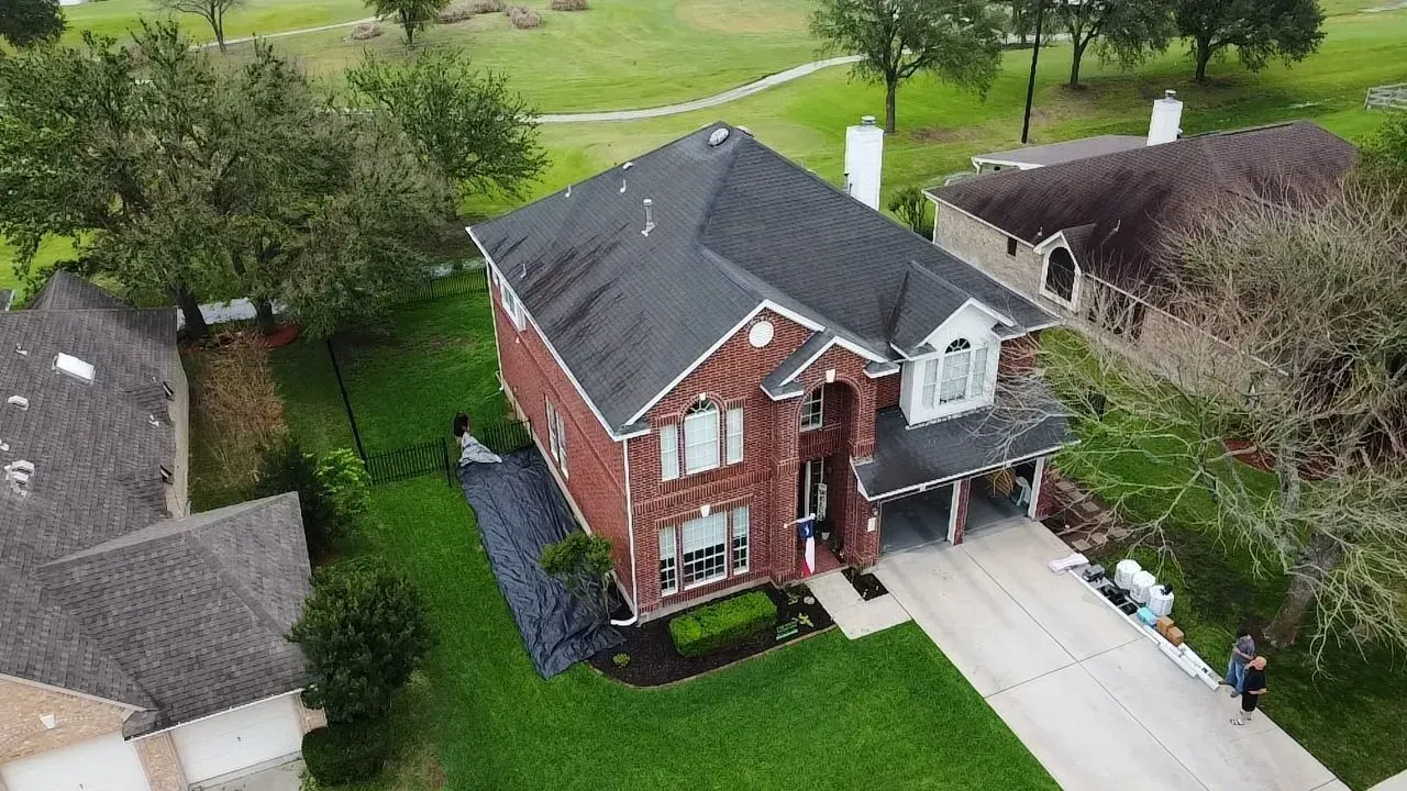 An aerial view of a brick house with a black roof in a residential area.
