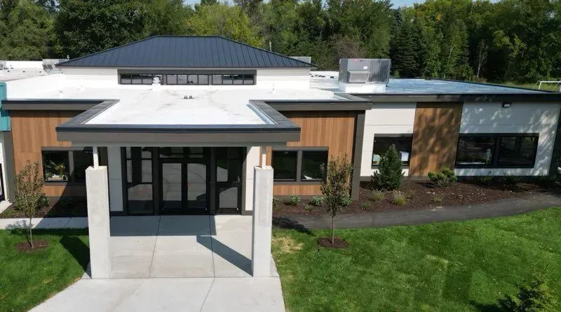 An aerial view of a modern house with a black roof surrounded by trees.