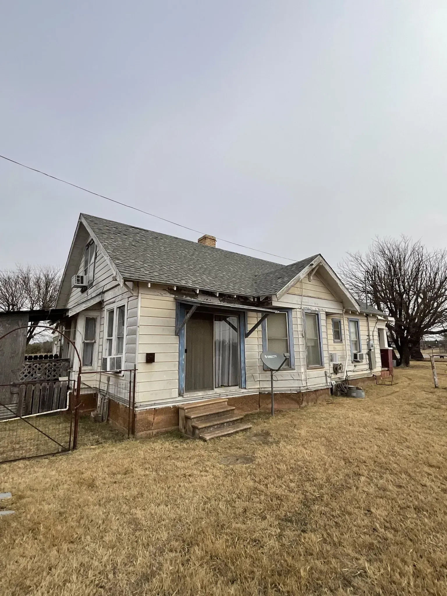 An old white house with a gray roof is sitting in the middle of a field.
