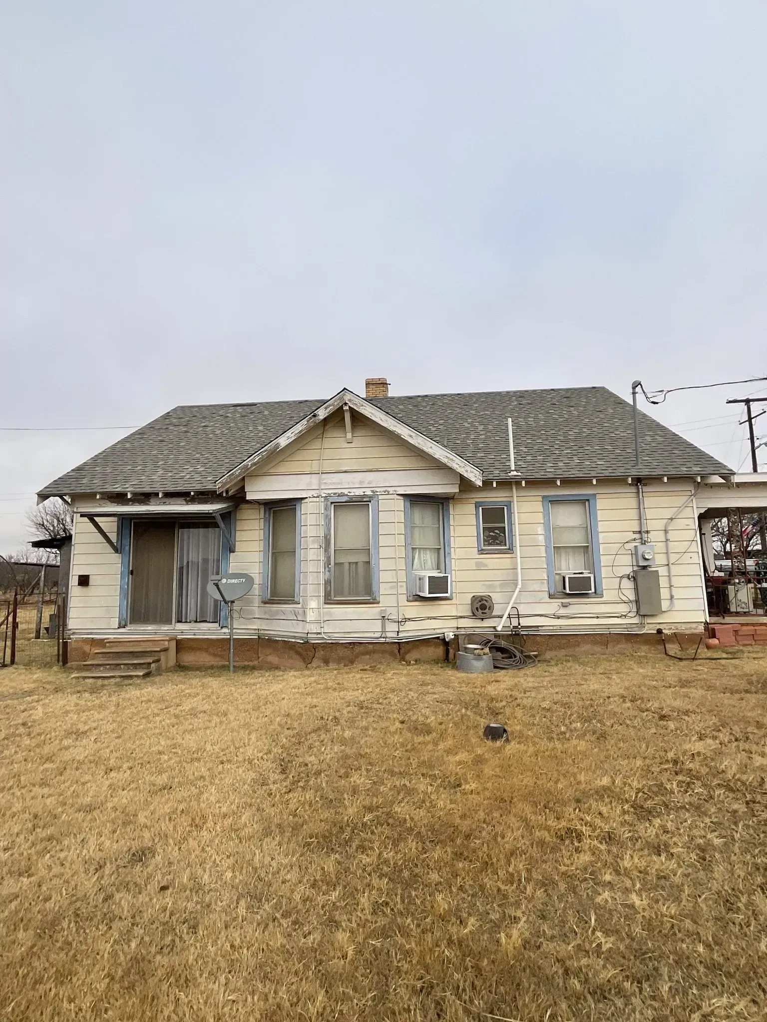 An old white house with a gray roof is sitting in the middle of a field.
