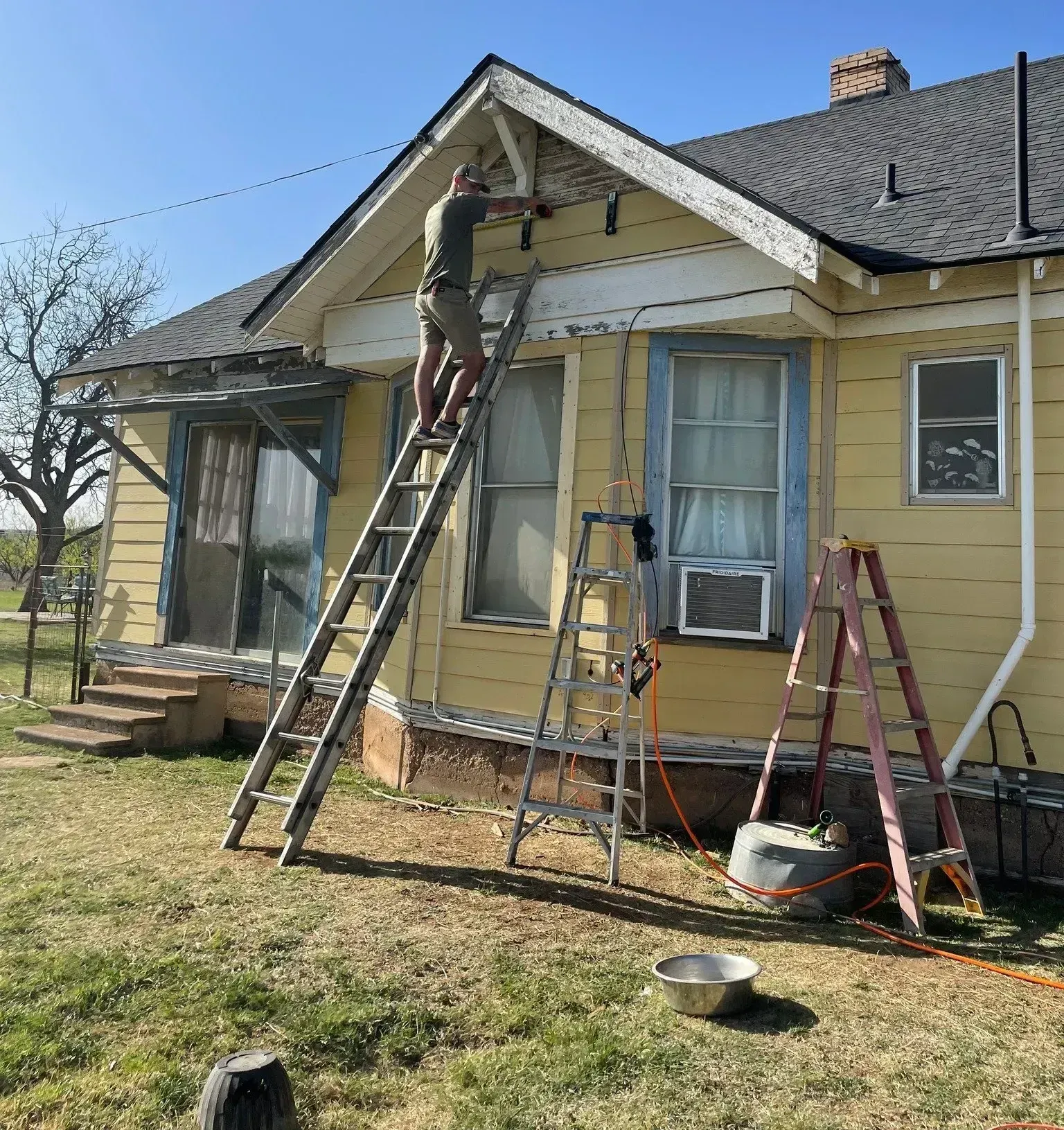 A man is standing on a ladder in front of a yellow house.