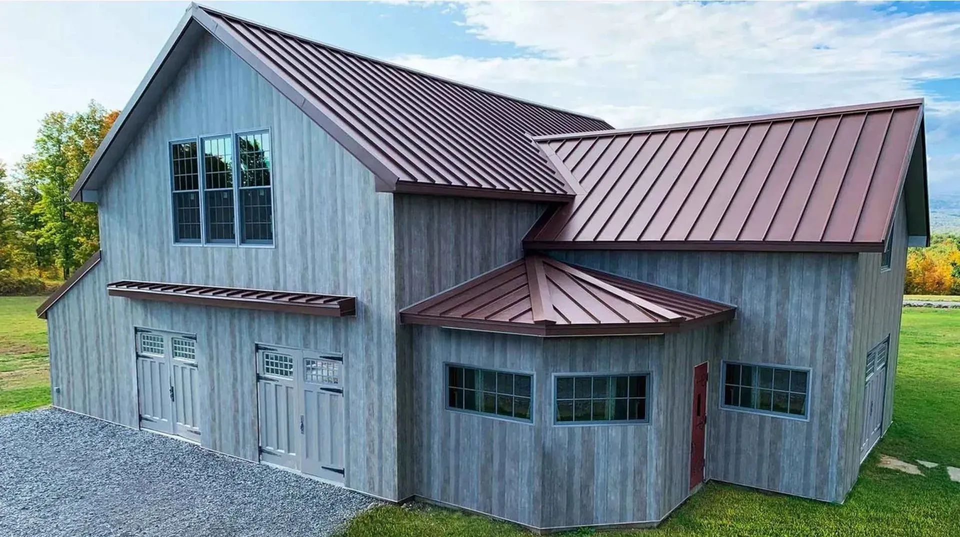 Two-story gray barn with brown metal roof and accents, featuring garage doors.
