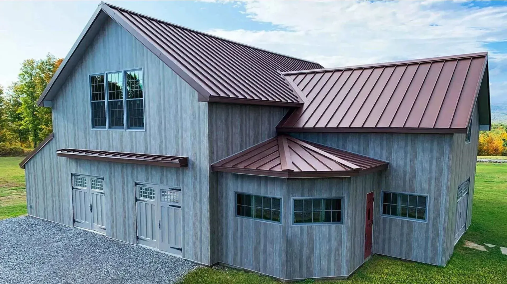 A large white barn with a brown roof is sitting in the middle of a grassy field.