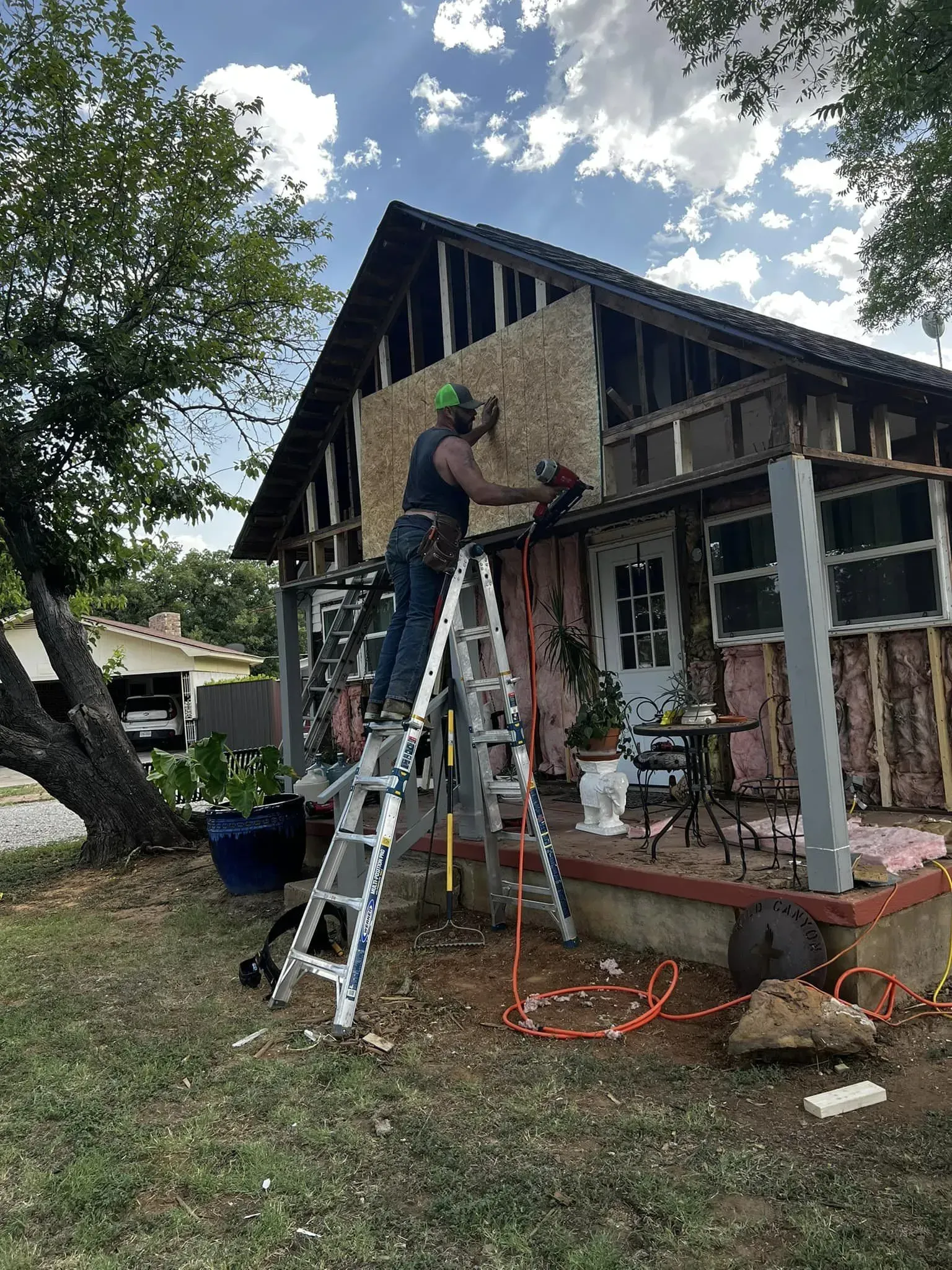 A man is standing on a ladder in front of a house.