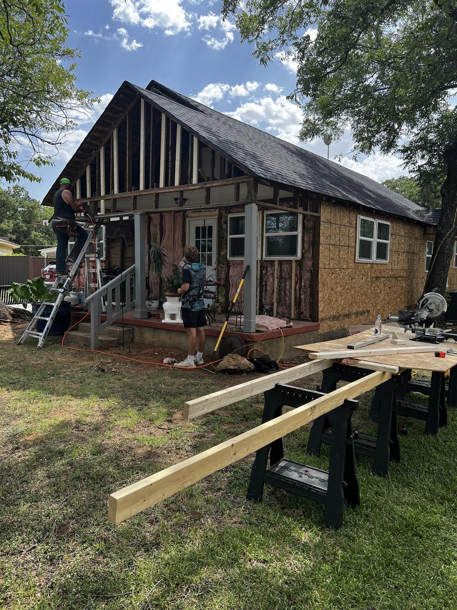A man is standing on a ladder in front of a house under construction.