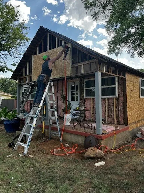 A man on a ladder is working on the side of a house.