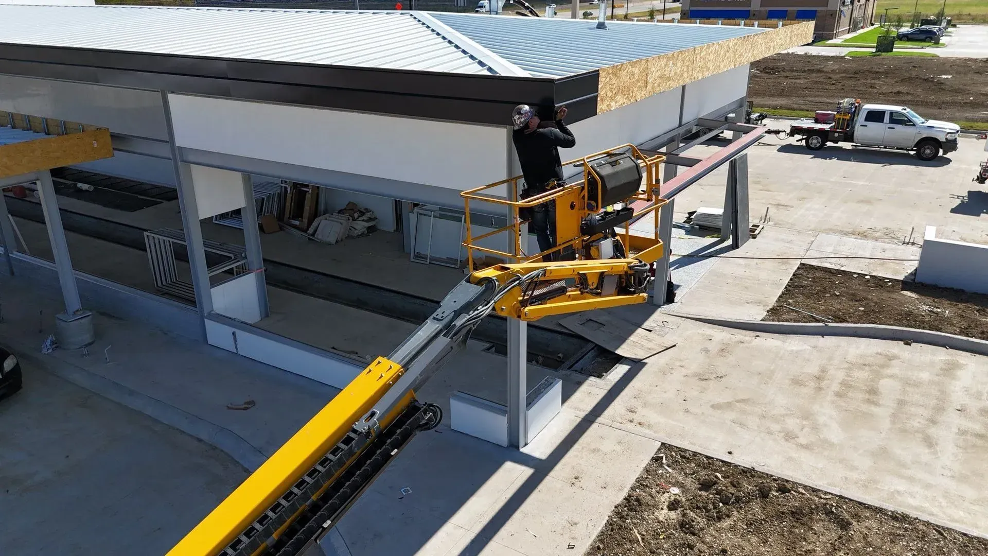 A man is standing on a lift working on the roof of a building.