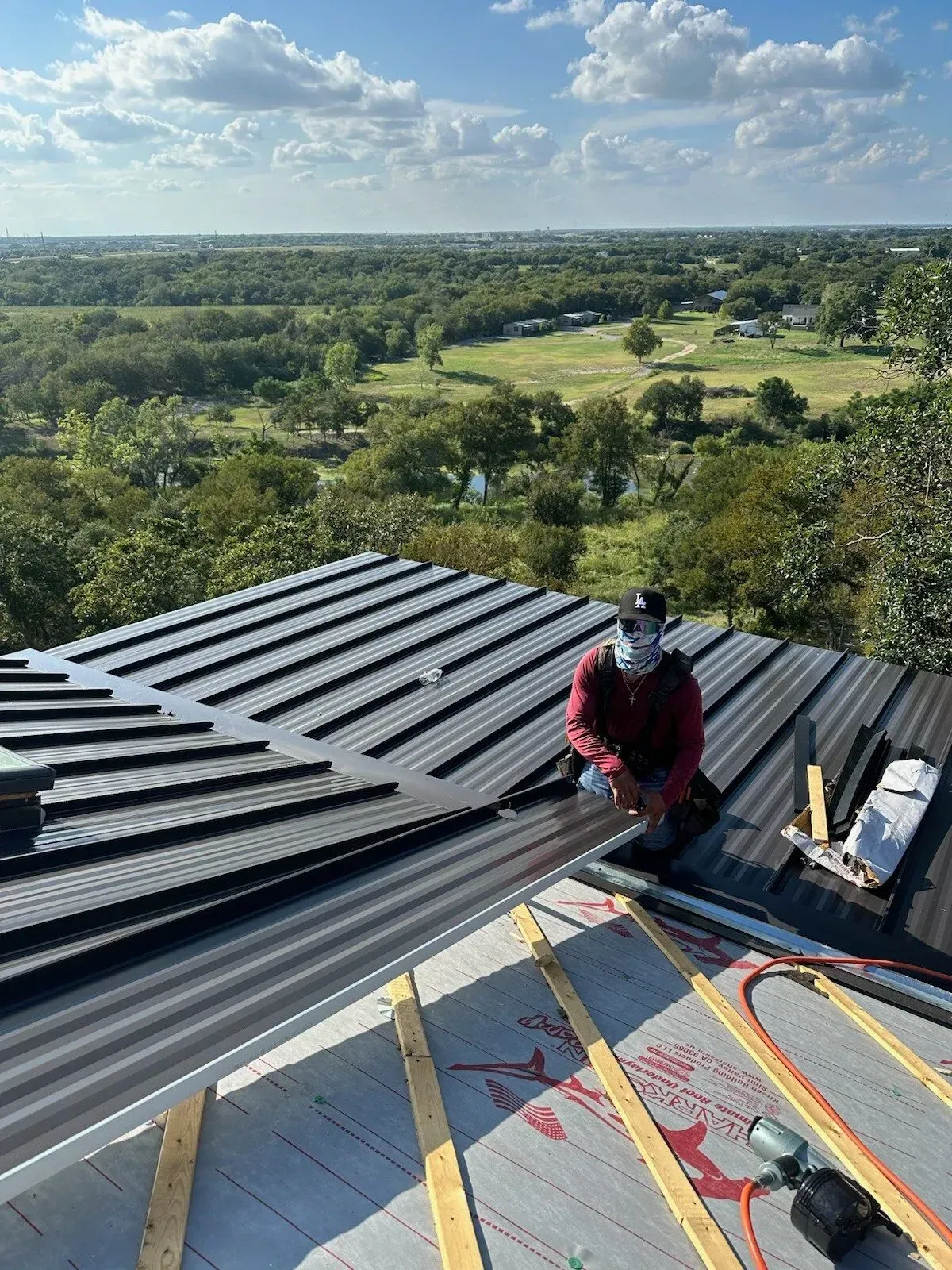 A man is sitting on top of a roof working on it.