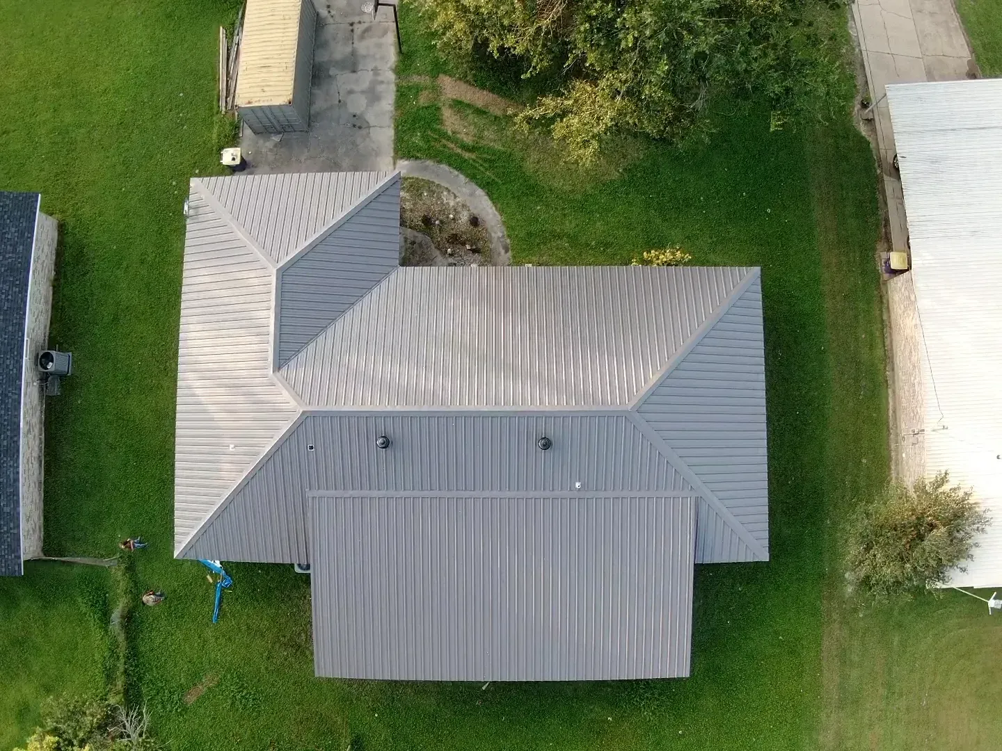 An aerial view of a house with a metal roof surrounded by grass and trees.