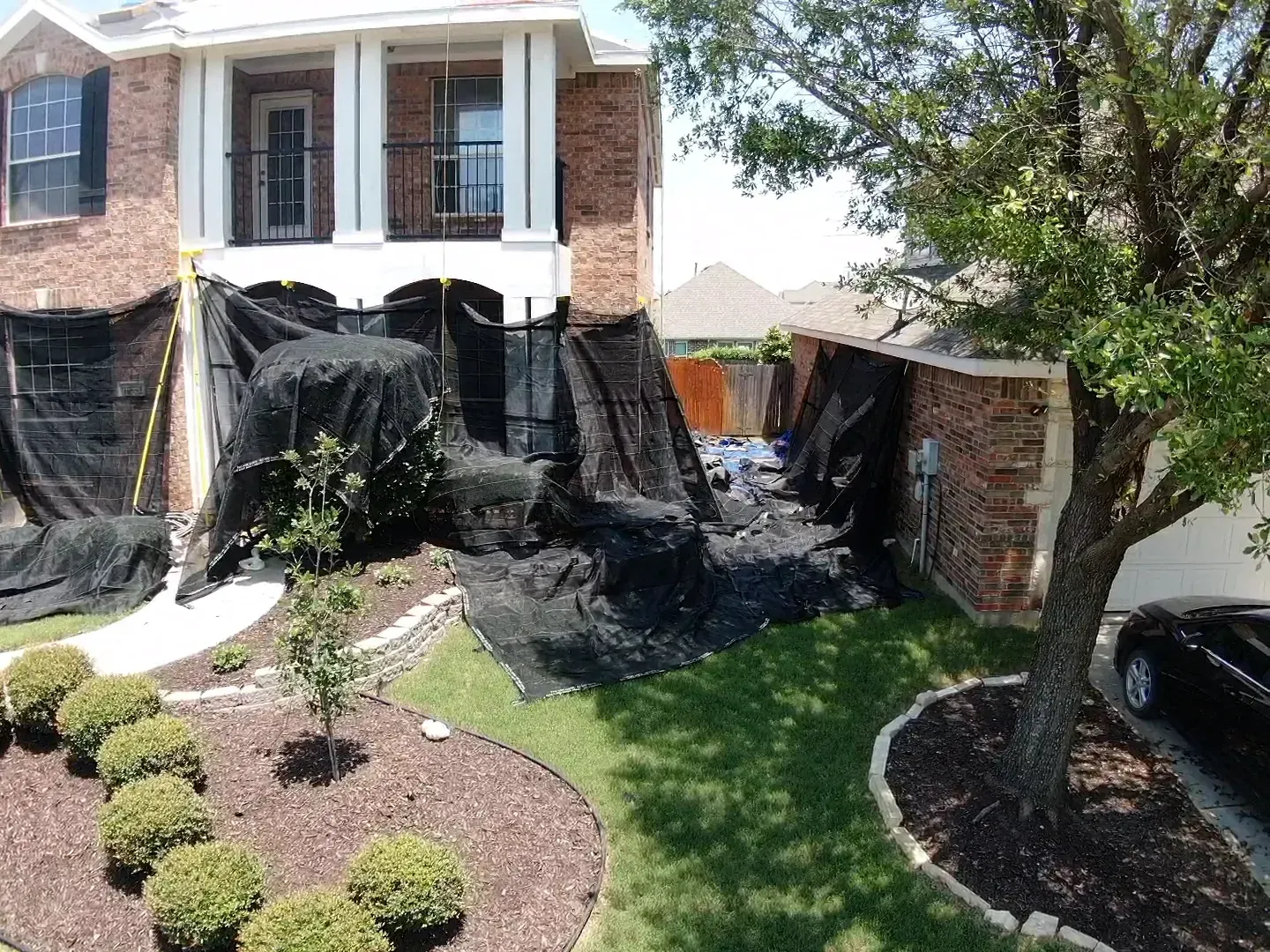 A brick house with a car parked in front of it is covered in black tarps.